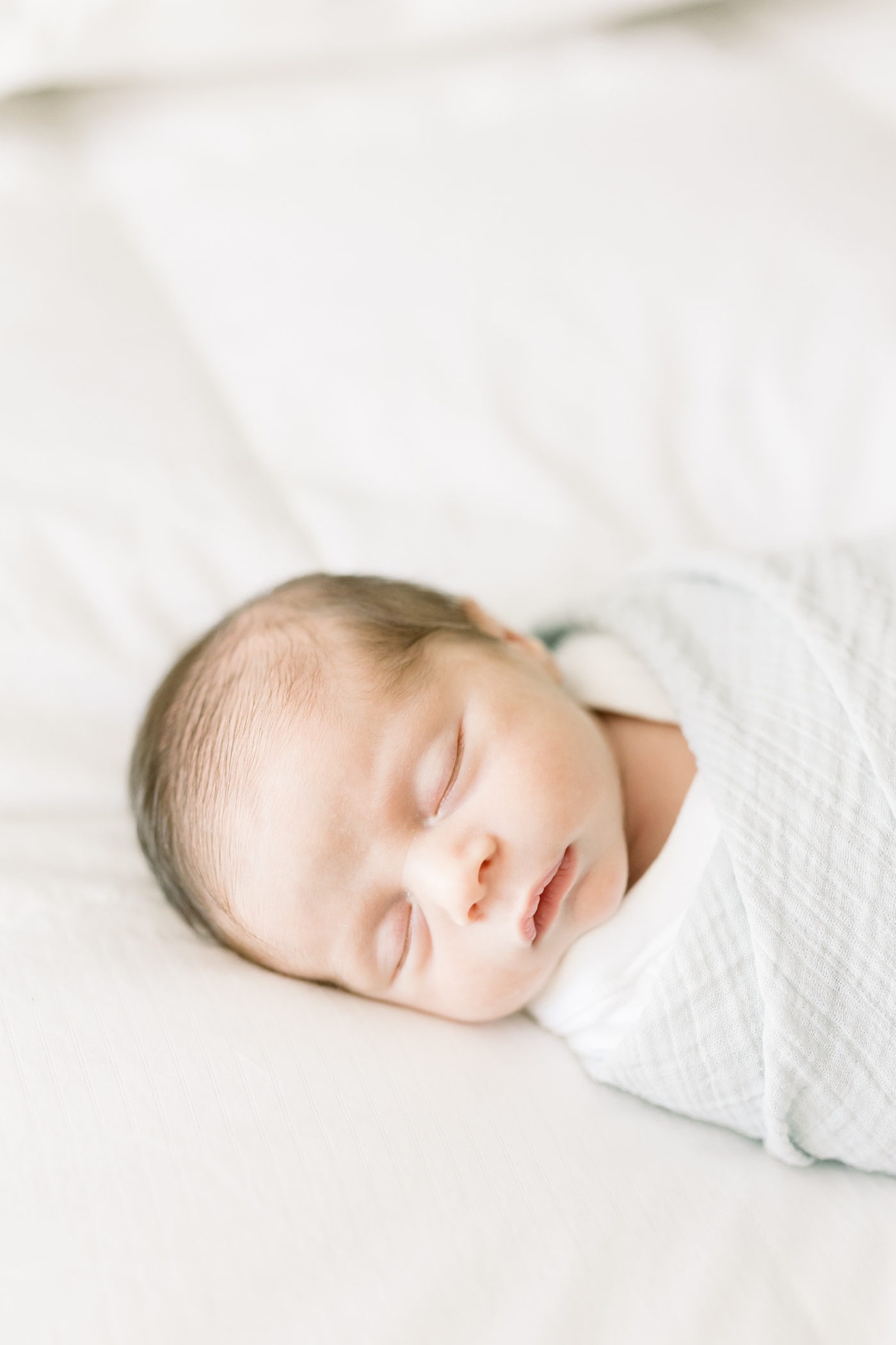 Sleeping newborn baby wrapped in a cream swaddle | Photo by Caitlyn Motycka Photography.
