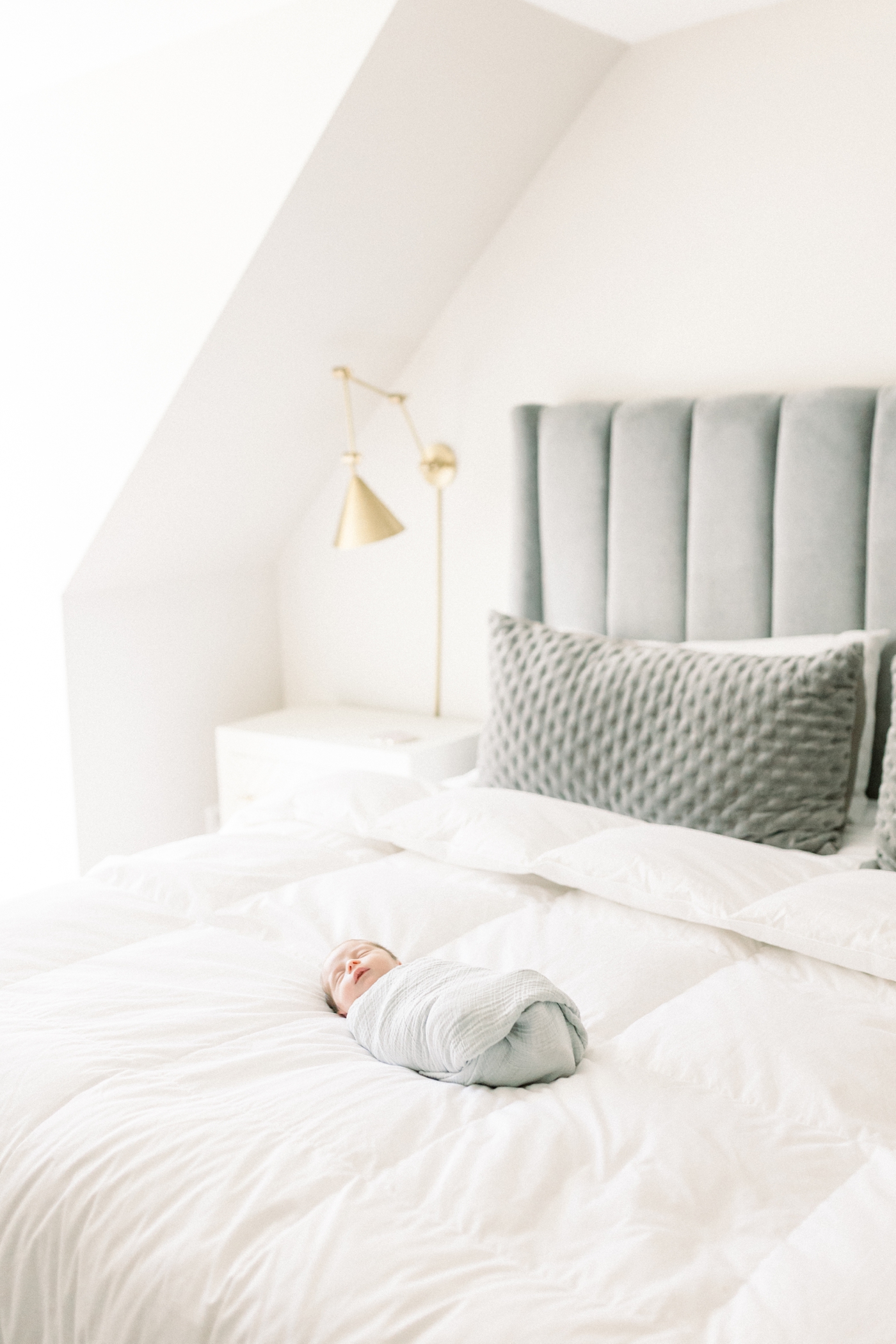 Newborn baby laying on a bed with a gray headboard | Photo by Caitlyn Motycka