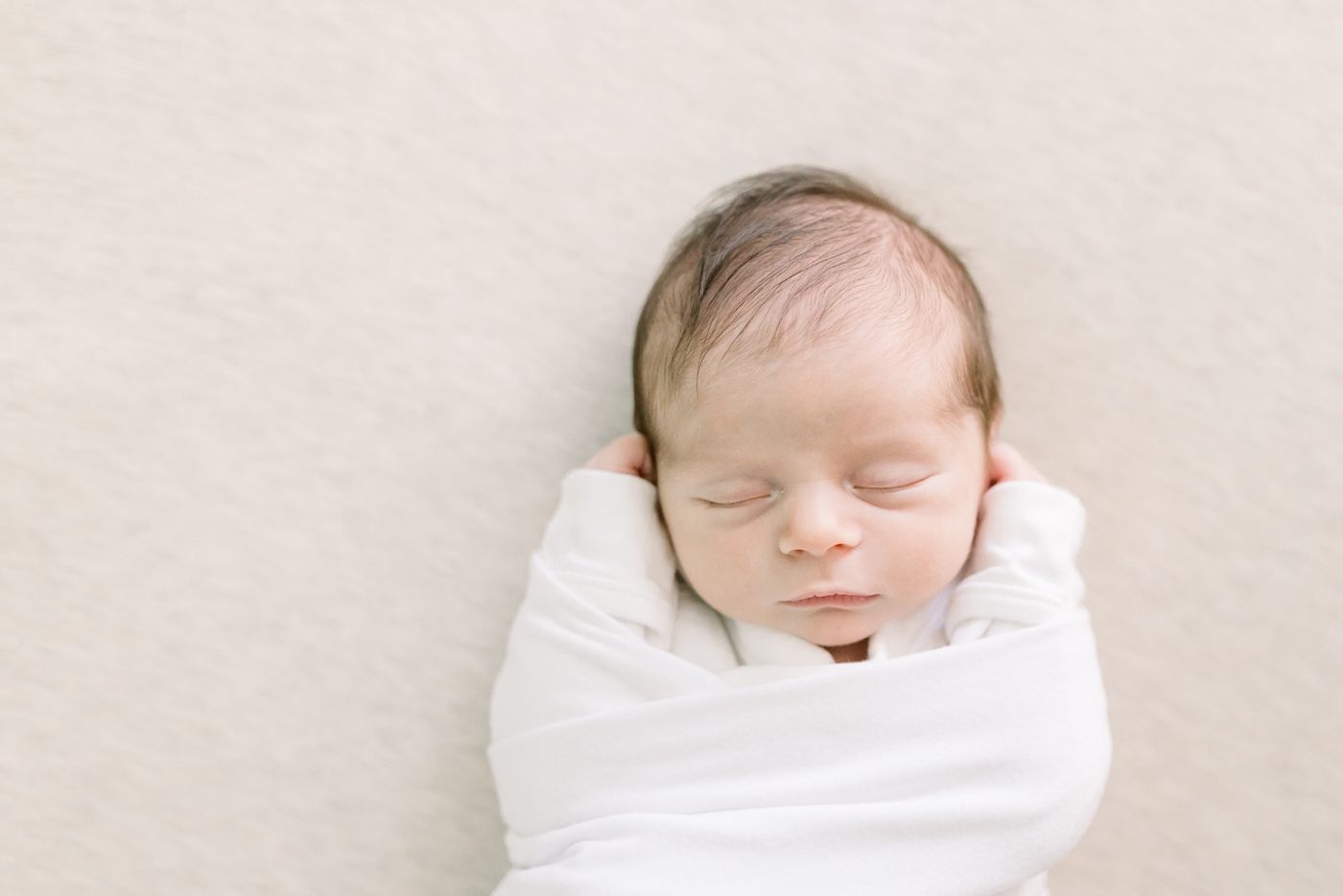 Sleeping newborn baby wrapped in a white swaddle | Photo by Caitlyn Motycka Photography.