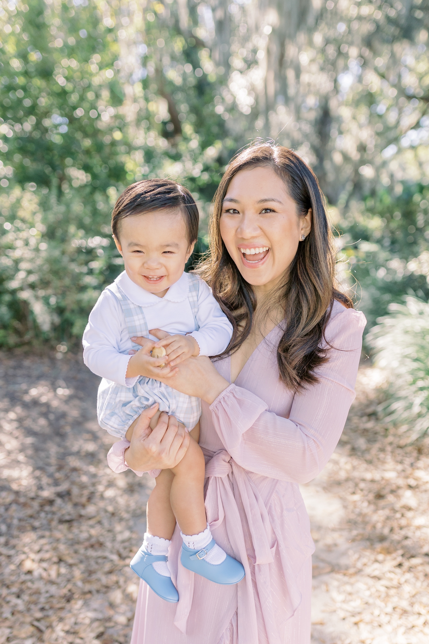 Baby boy and mom in pink dress smile for the camera in Hampton park | Photo by Caitlyn Motycka Photography