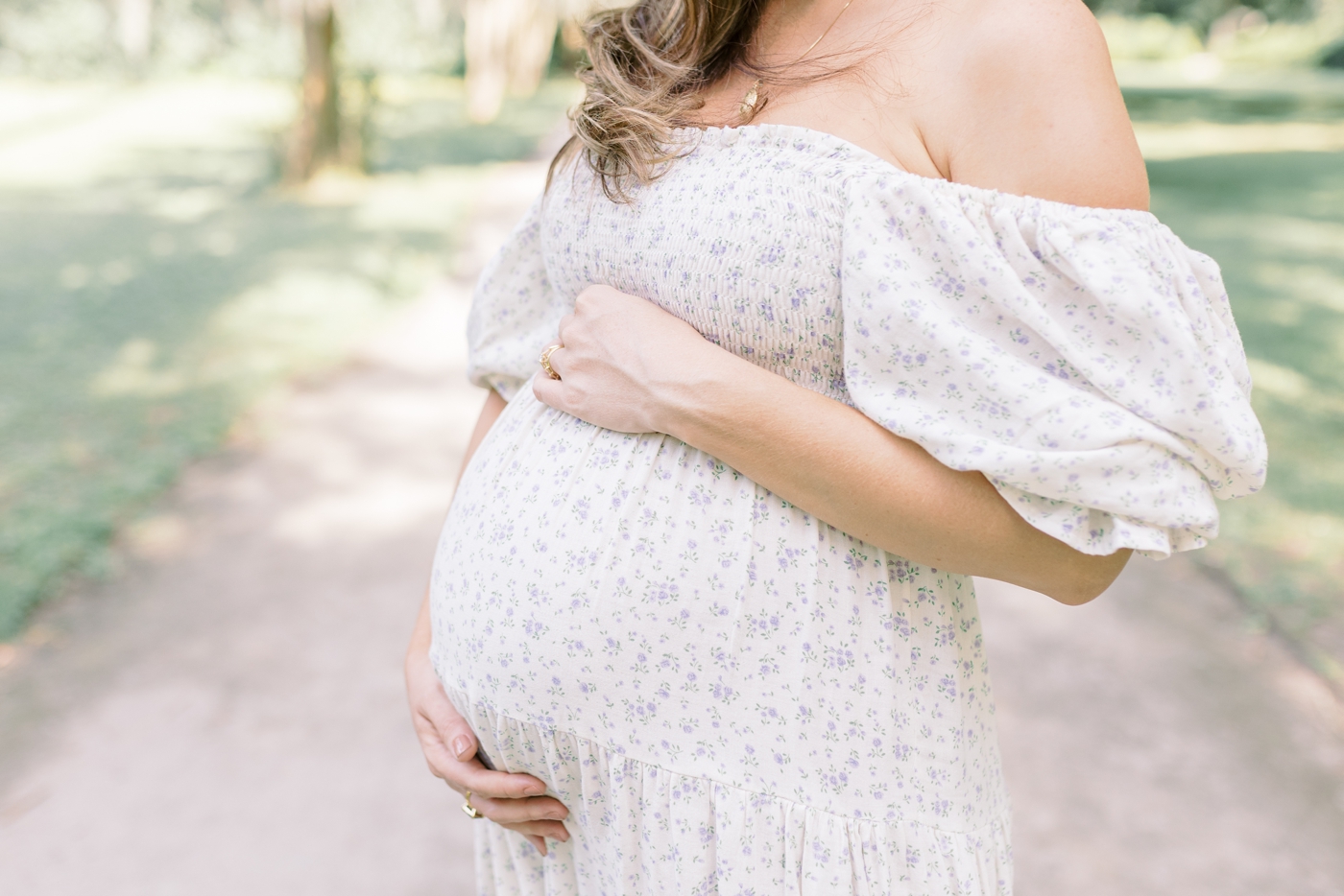 Mom to be cradling her belly in floral print dress | Photo by Caitlyn Motycka Photography.