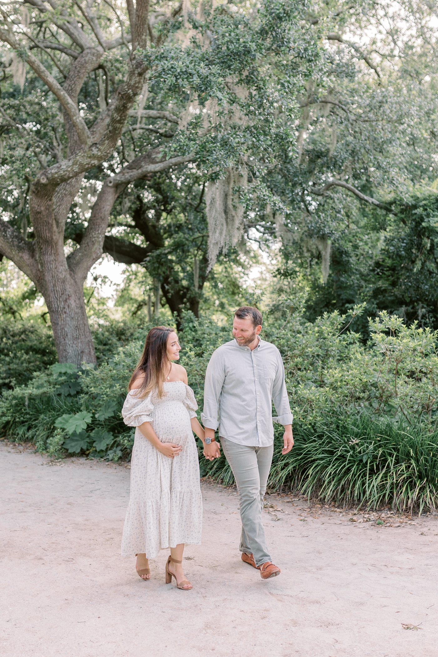 Mom and dad to be holding hands walking in Hampton Park | Photo by Caitlyn Motycka Photography.