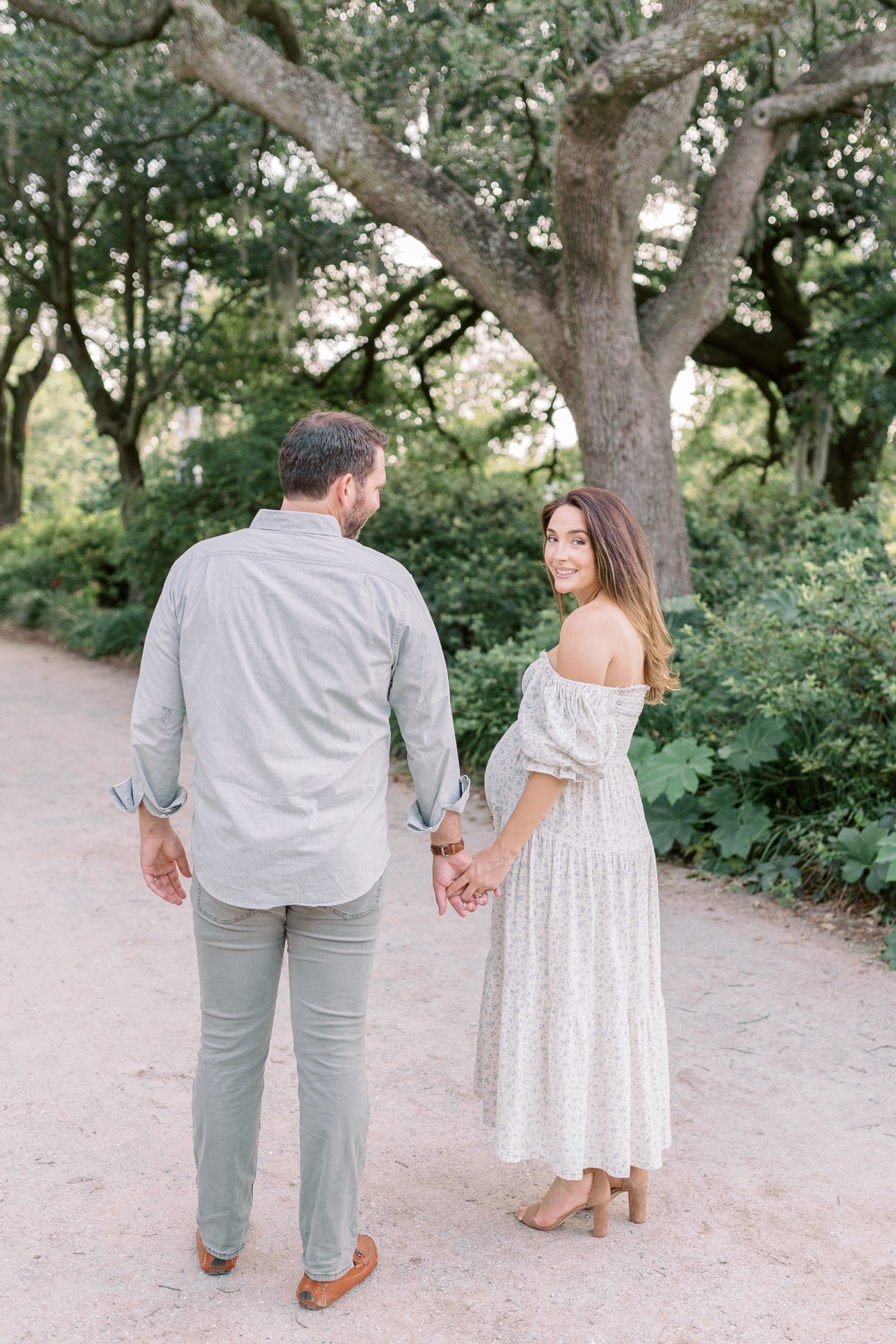 Mom and dad to be walking through a park in Charleston, SC | Photo by Caitlyn Motycka Photography.