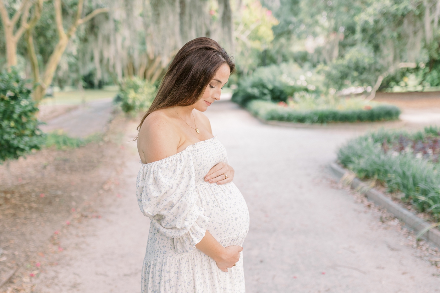 Mom to be holding her belly standing under Spanish moss | Photo by Caitlyn Motycka Photography.