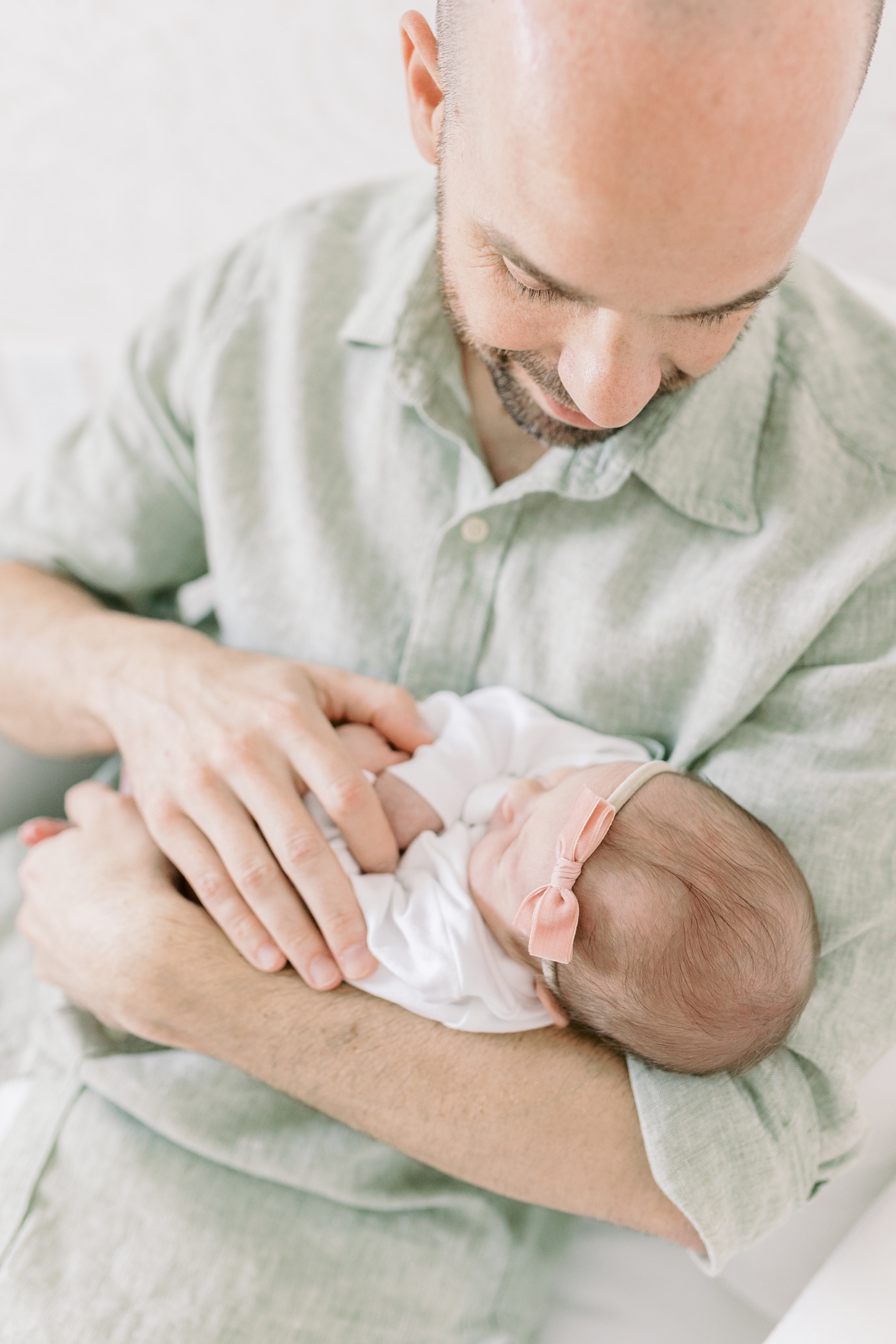 Dad in green shirt holding newborn baby girl with pink bow | Photo by Caitlyn Motycka Photography.