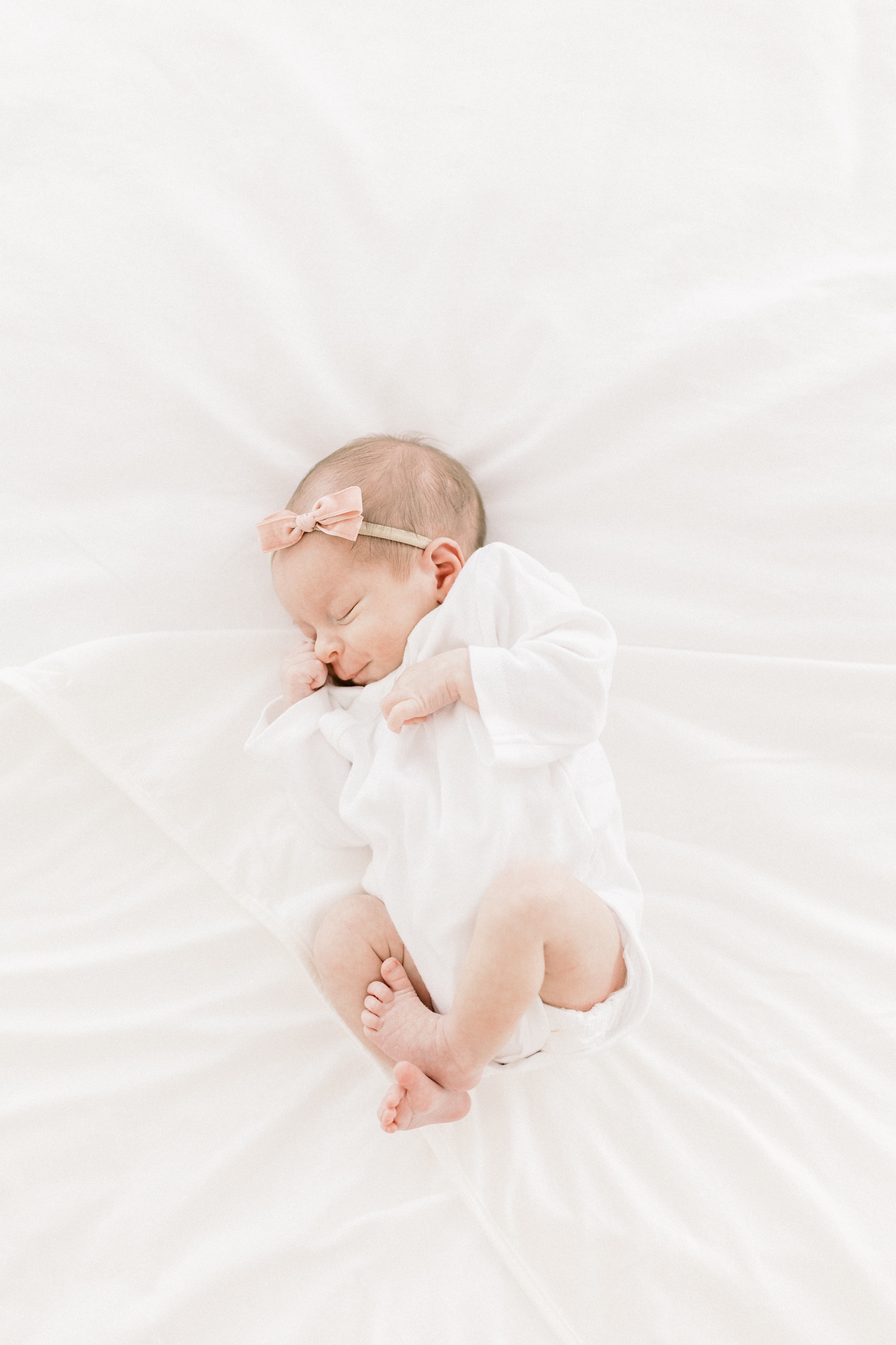 Newborn baby in white onesie wearing a pink bow | Photo by Caitlyn Motycka Photography.