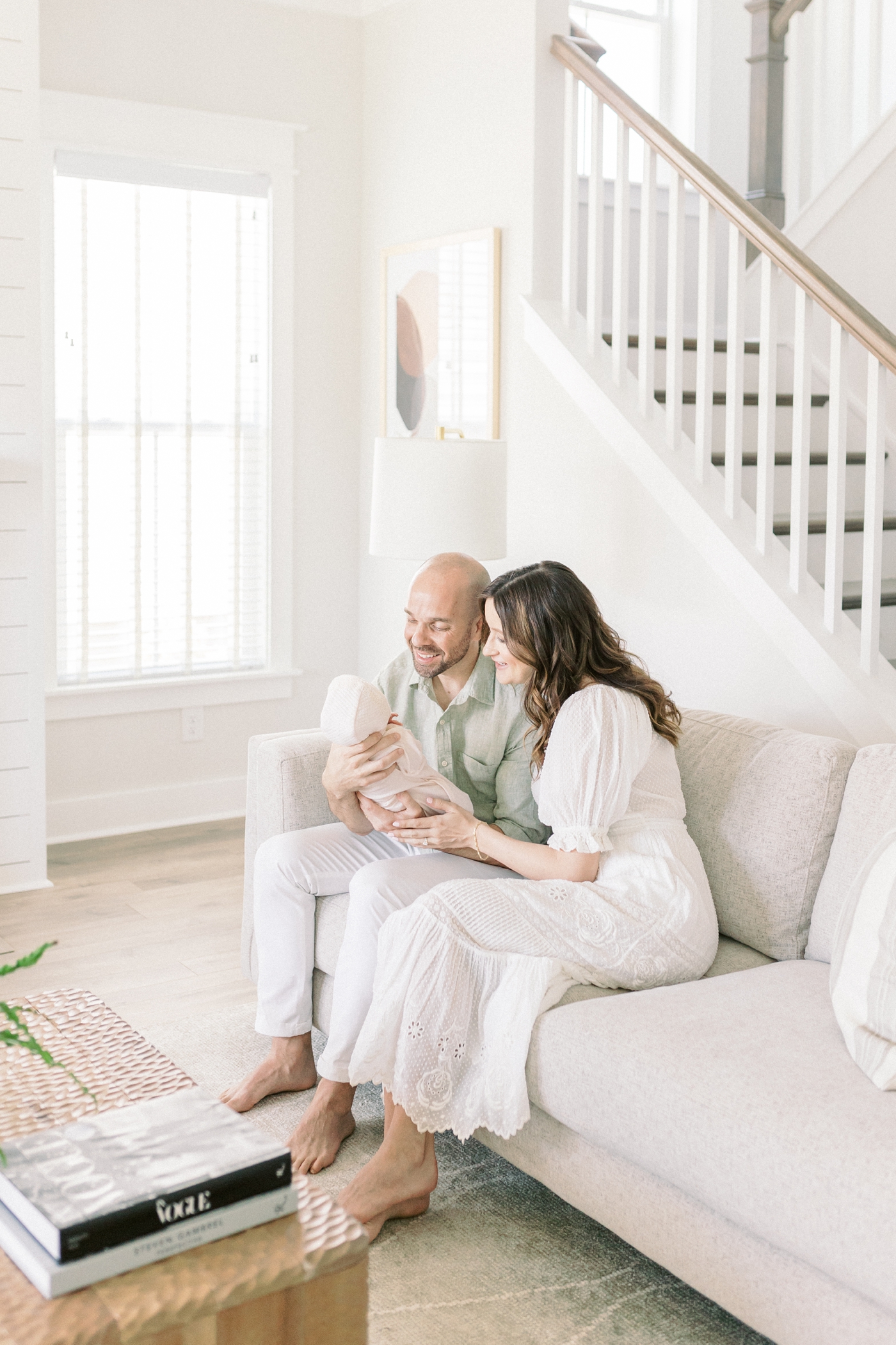 Mom and dad holding their baby girl sitting on their couch during their lifestyle newborn session | Photo by Caitlyn Motycka Photography