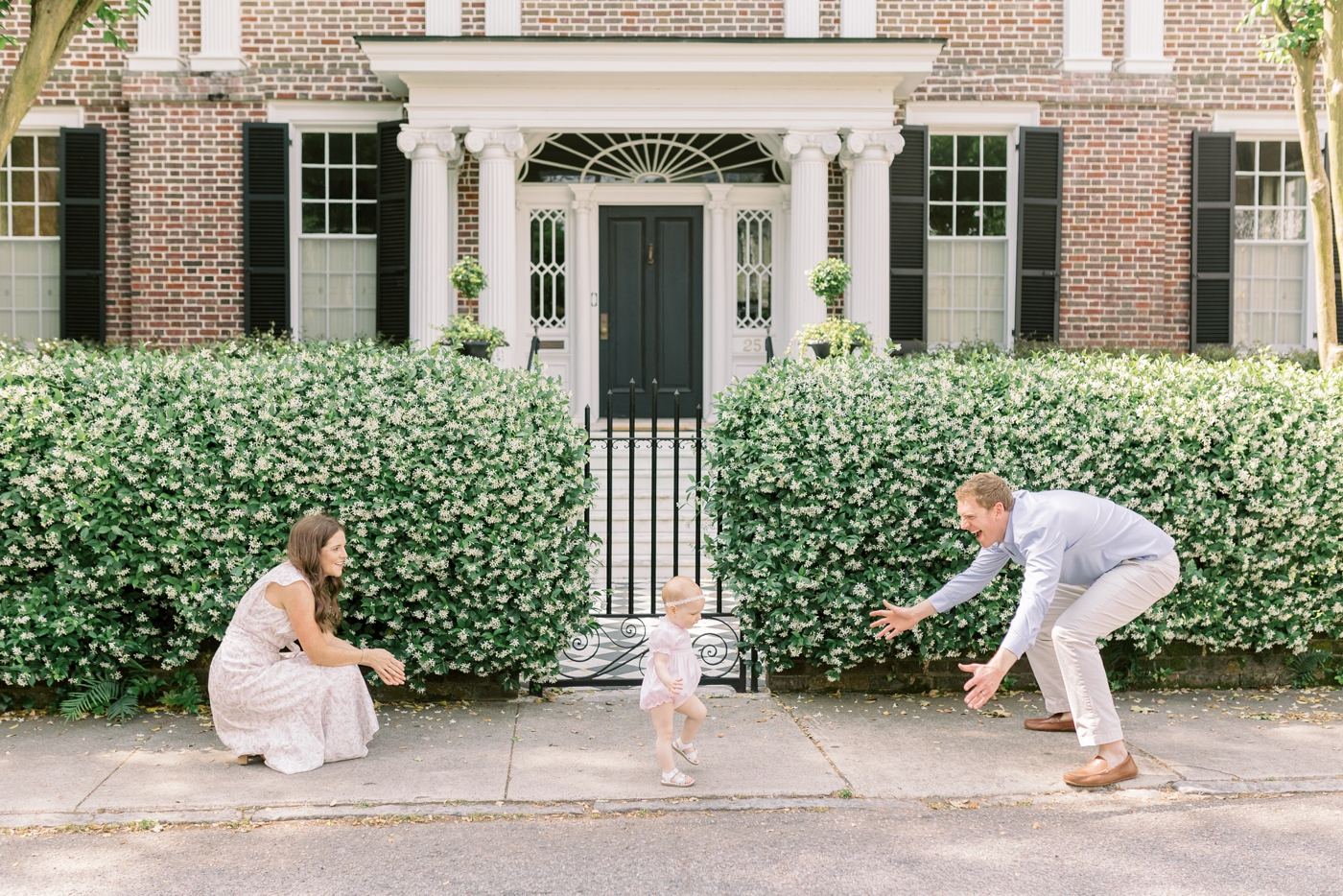 Baby daughter walking toward dad on the sidewalk while mom watches during her 18month session | Photo by Caitlyn Motycka Photography.