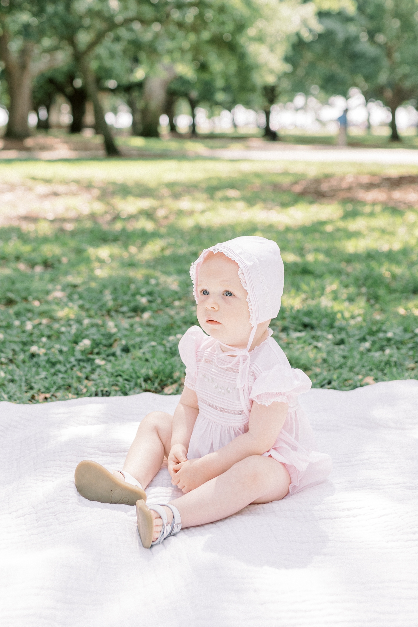Baby girl in pink bubble and bonnet sitting in White Point Garden | Photo by Caitlyn Motycka Photography.