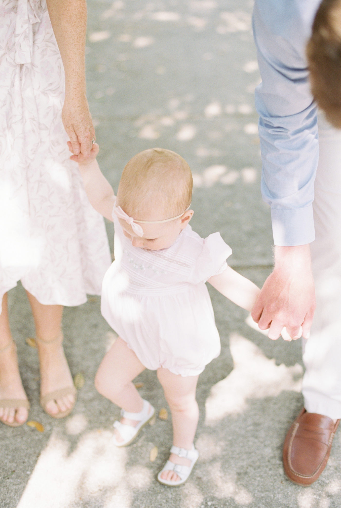 Baby girl with pink headband holding mom and dad's hands | Photo by Caitlyn Motycka Photography.