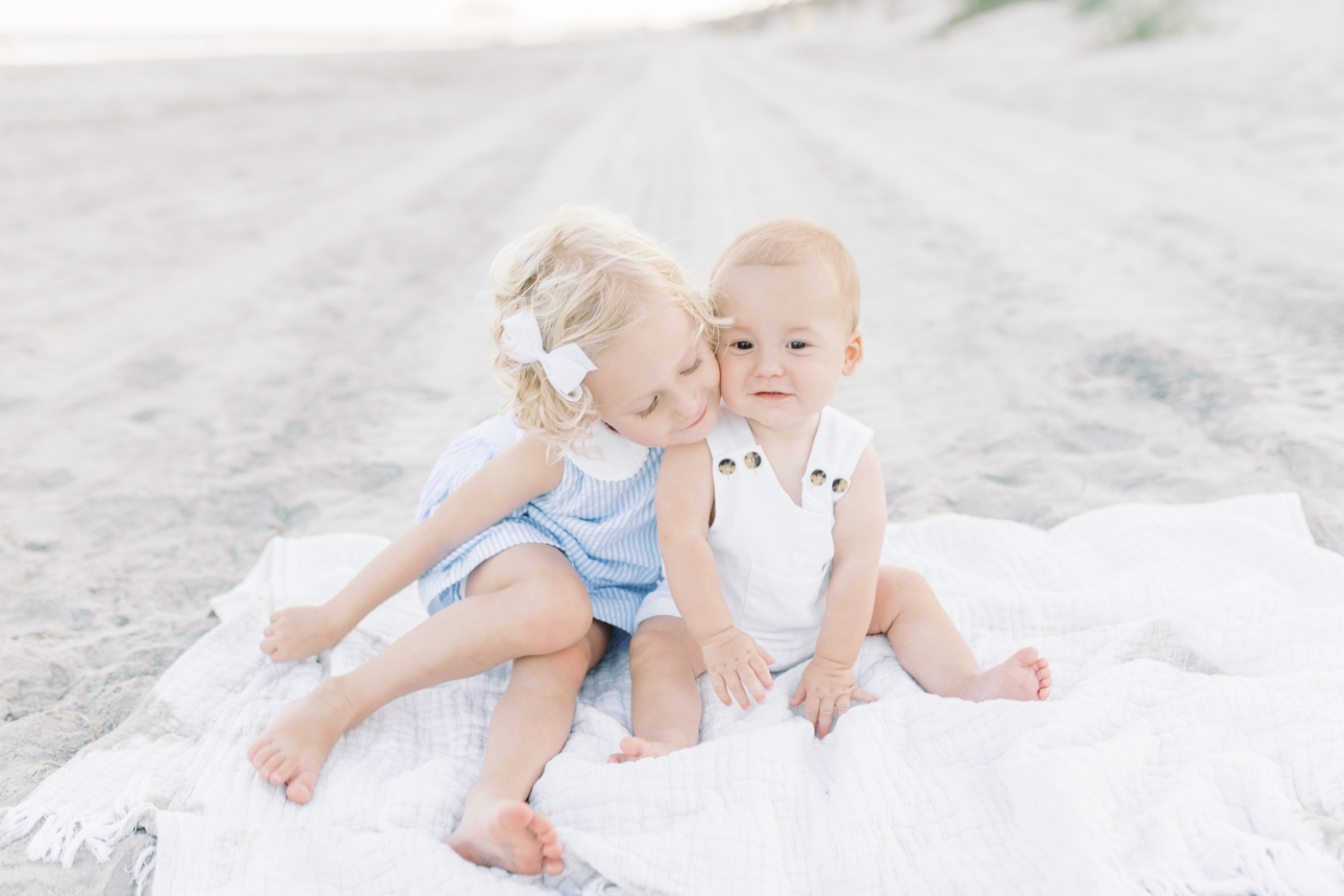 Sister snuggling her little brother on the beach | Photo by Caitlyn Motycka Photography.