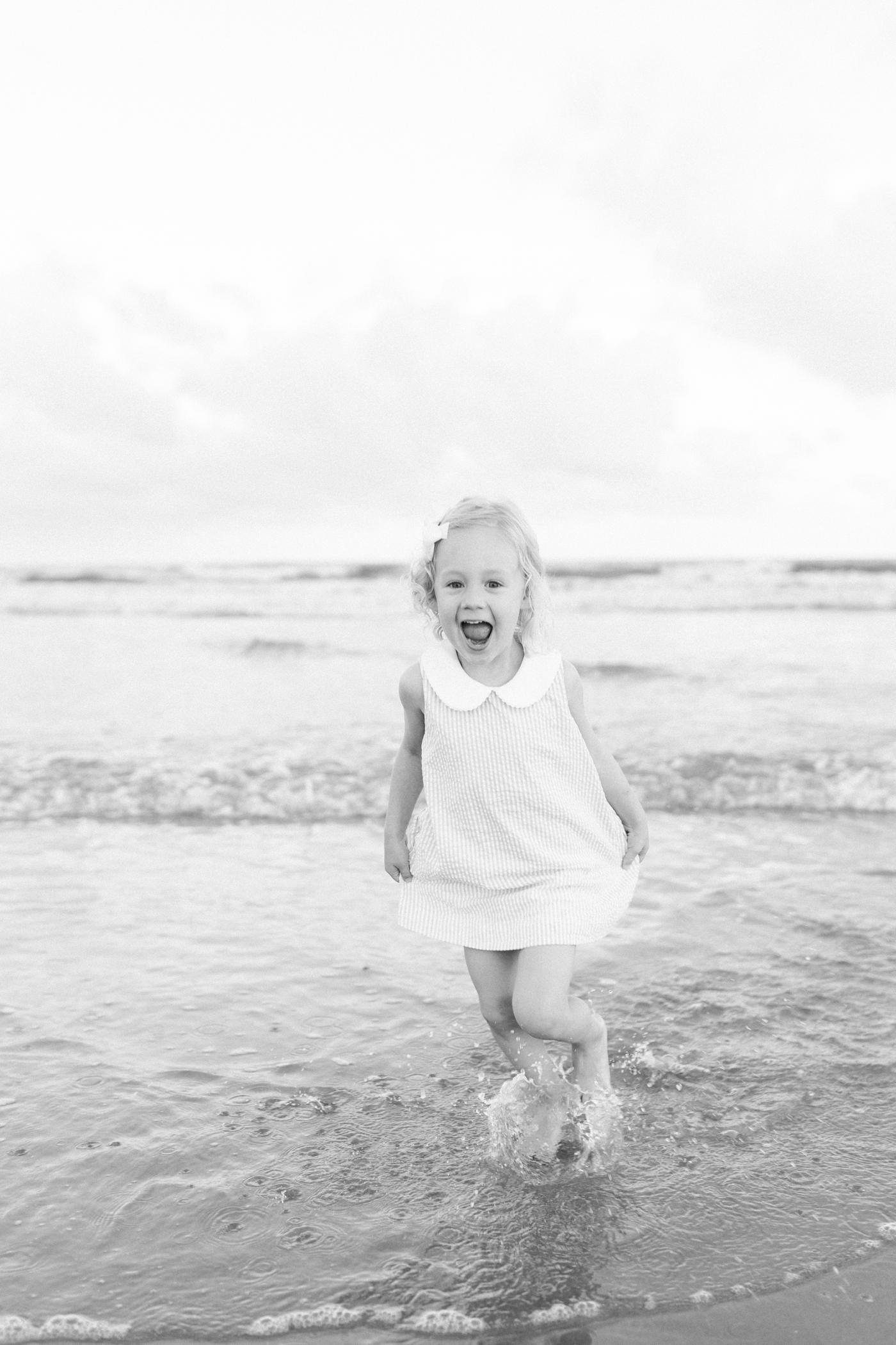 Little girl in striped dress playing in the ocean during isle of palms beach session| Photo by Caitlyn Motycka Photography.