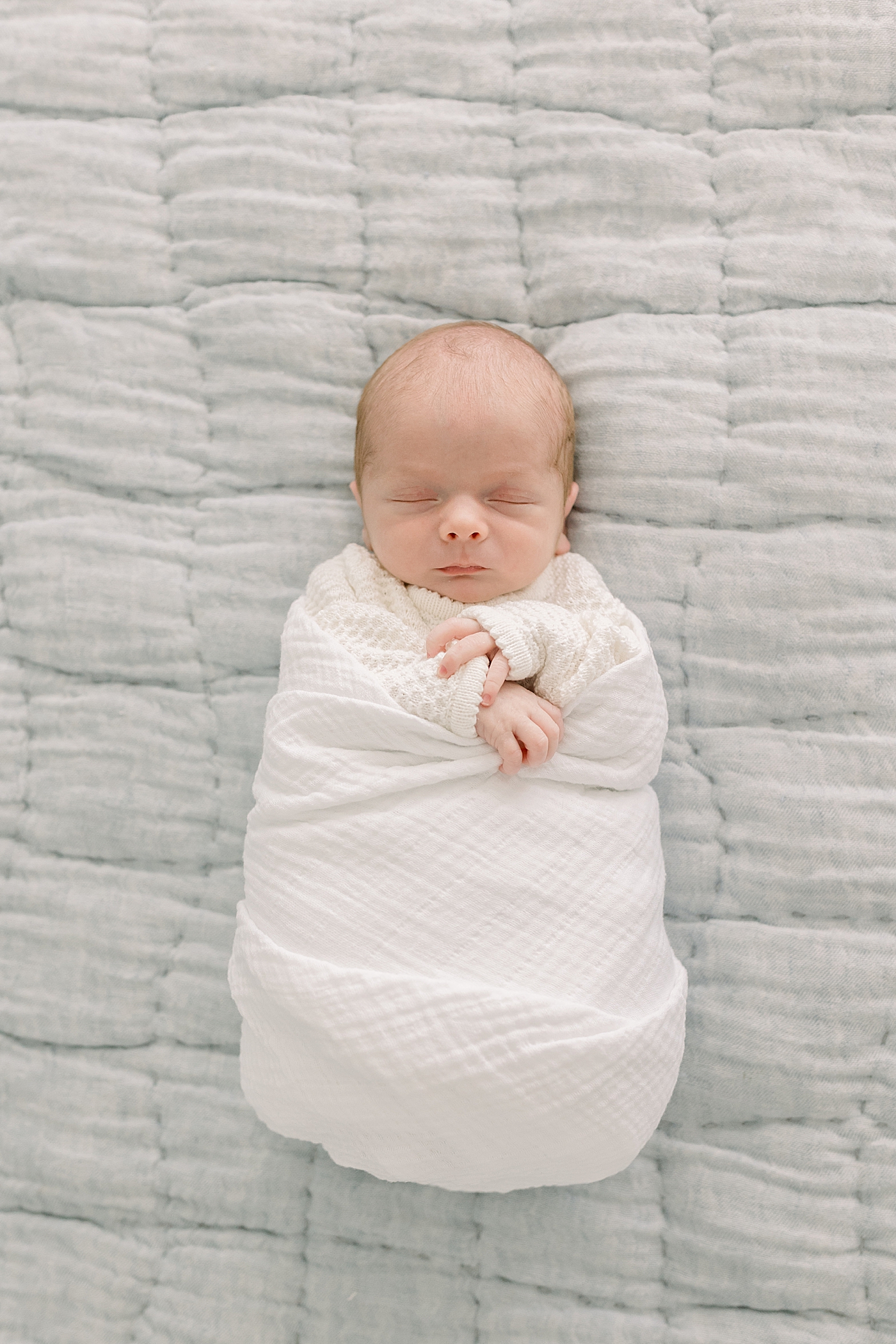 Baby boy wrapped in a white swaddle sleeping on a gray background | Photo by Caitlyn Motycka Photography