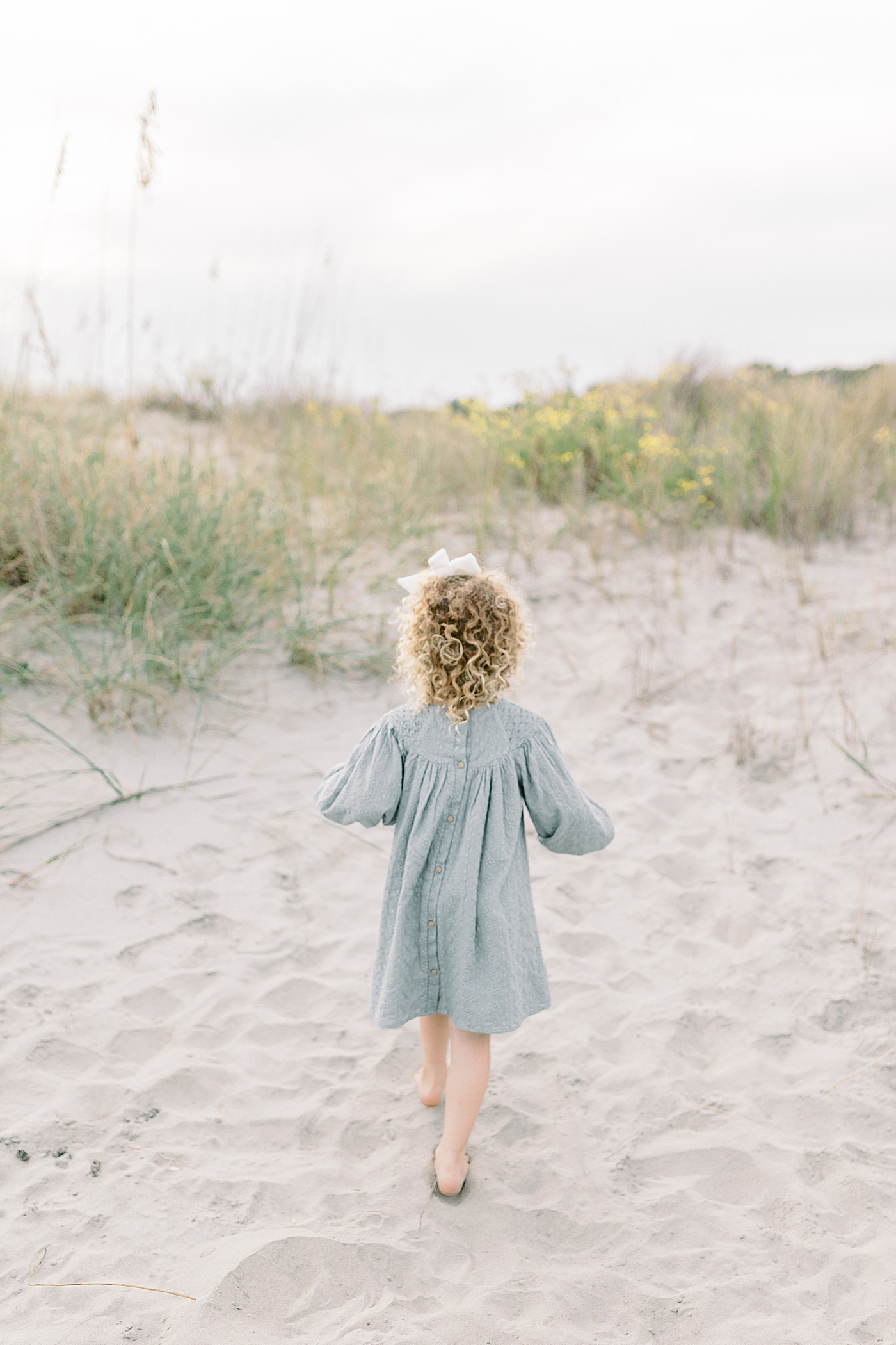 Little girl in a blue dress walking near the sand dunes | Photo by Caitlyn Motycka Photography