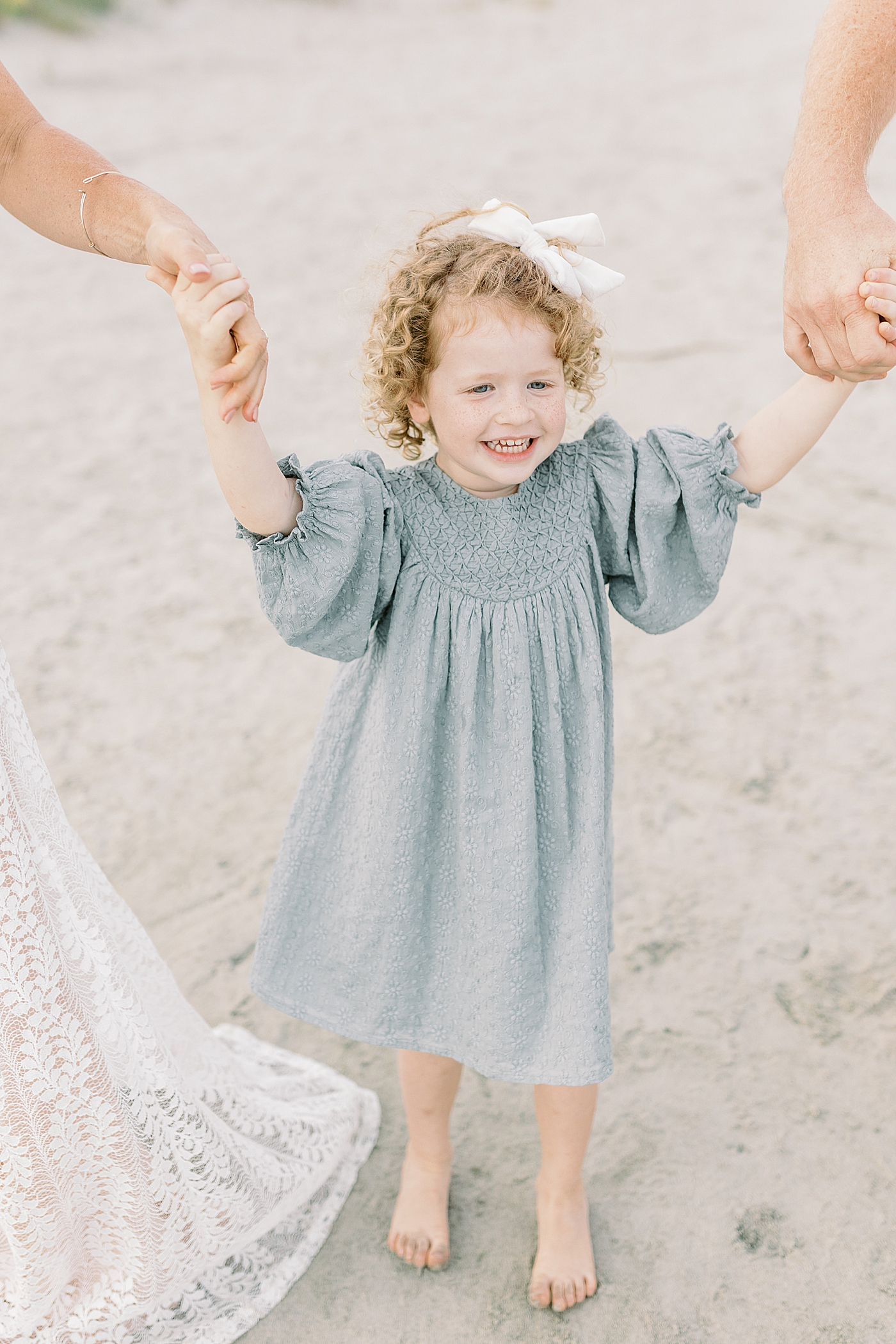 Little girl in light blue dress holding her mom and dad's hands | Photo by Caitlyn Motycka Photography