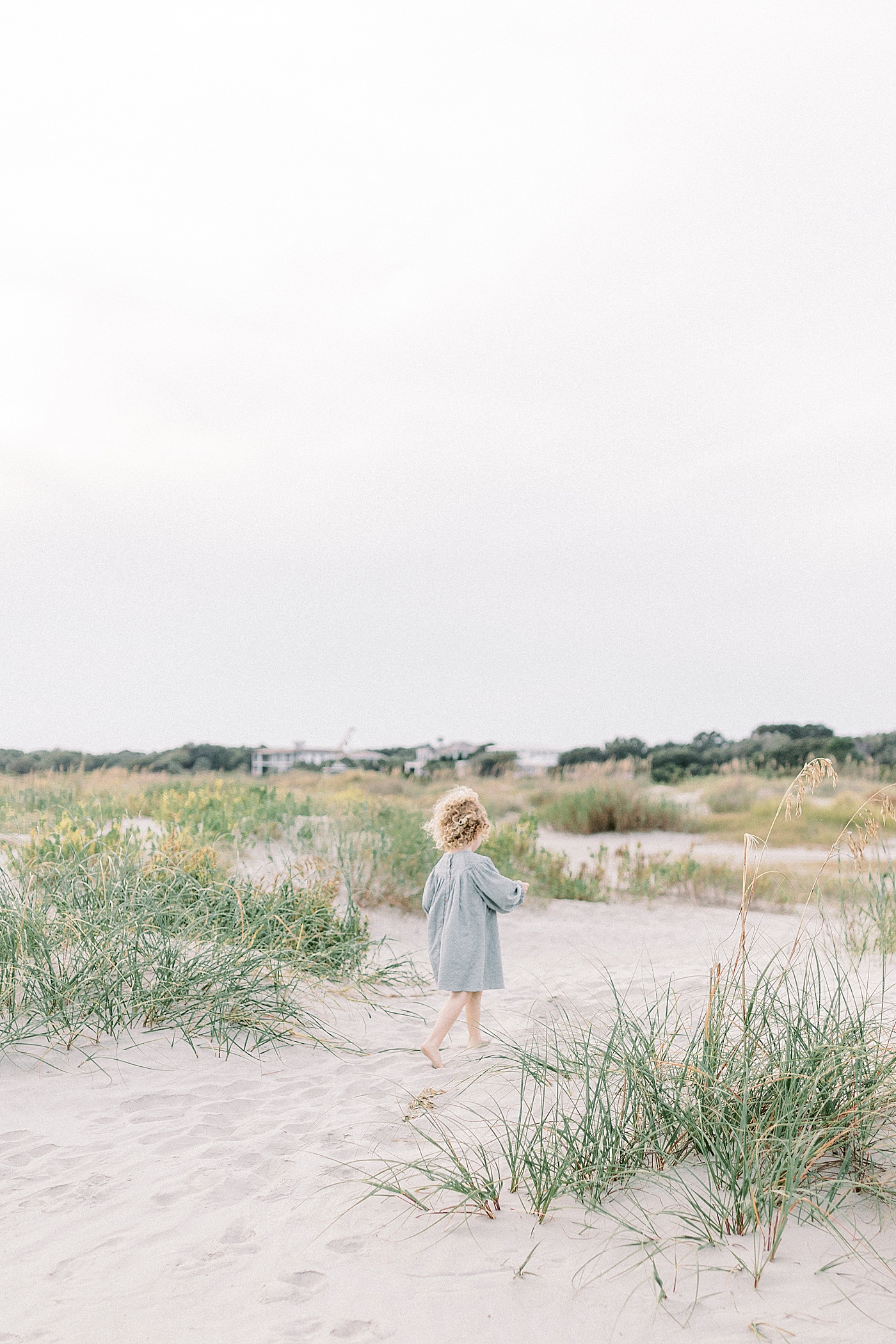 Little girl in blue dress walking on the beach near sand dunes | Photo by Caitlyn Motycka Photography
