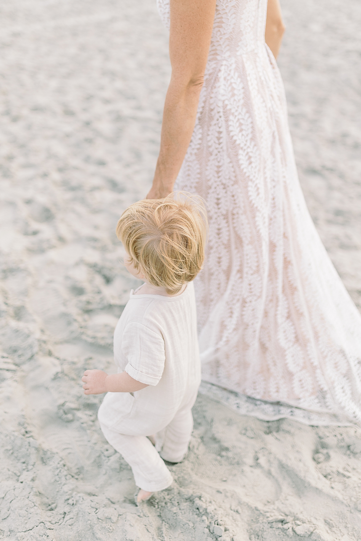 Toddler boy in white holding moms hand during fall family session at beach | Photo by Caitlyn Motycka Photography