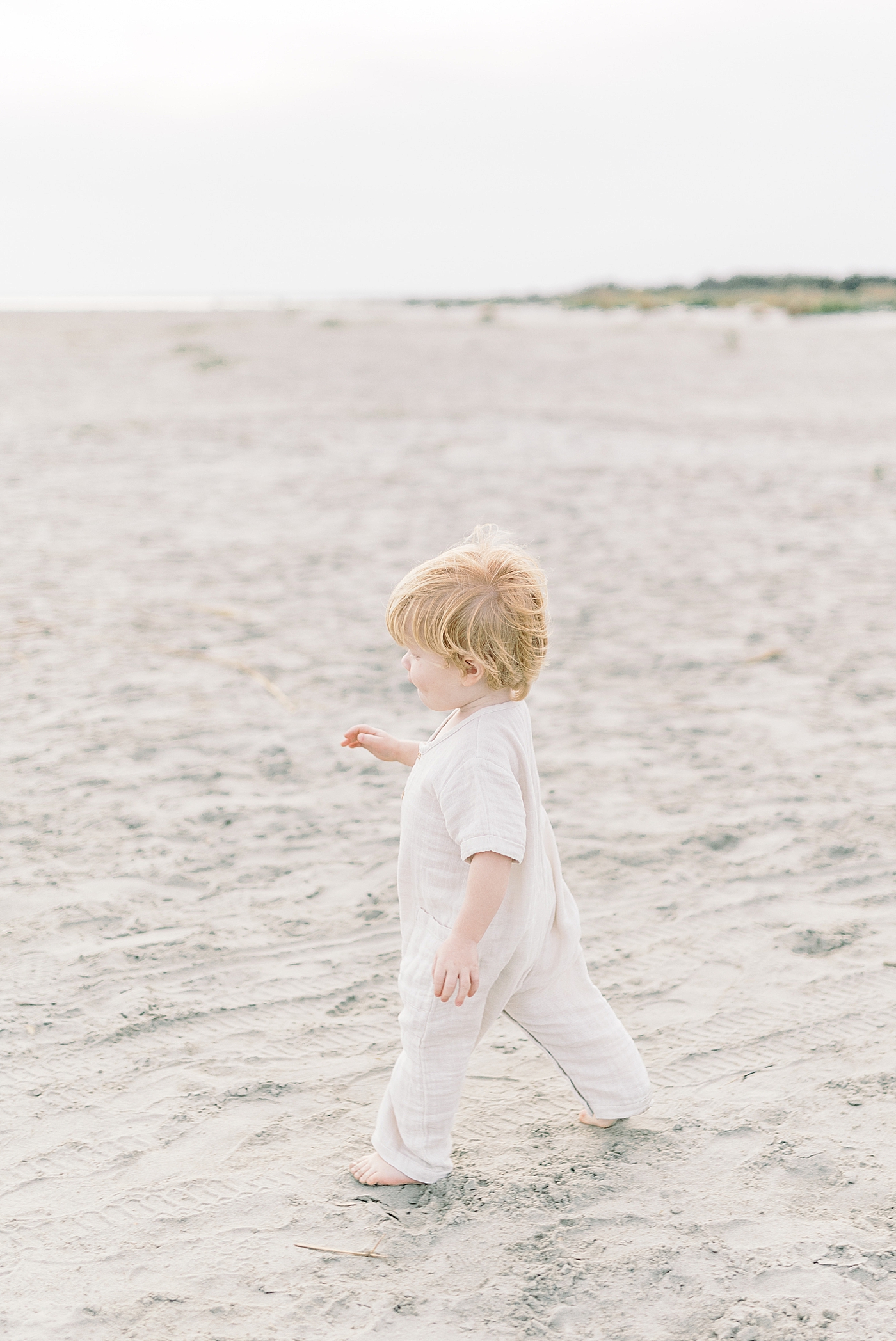 Blonde baby boy running on the beach during fall family session | Photo by Caitlyn Motycka Photography