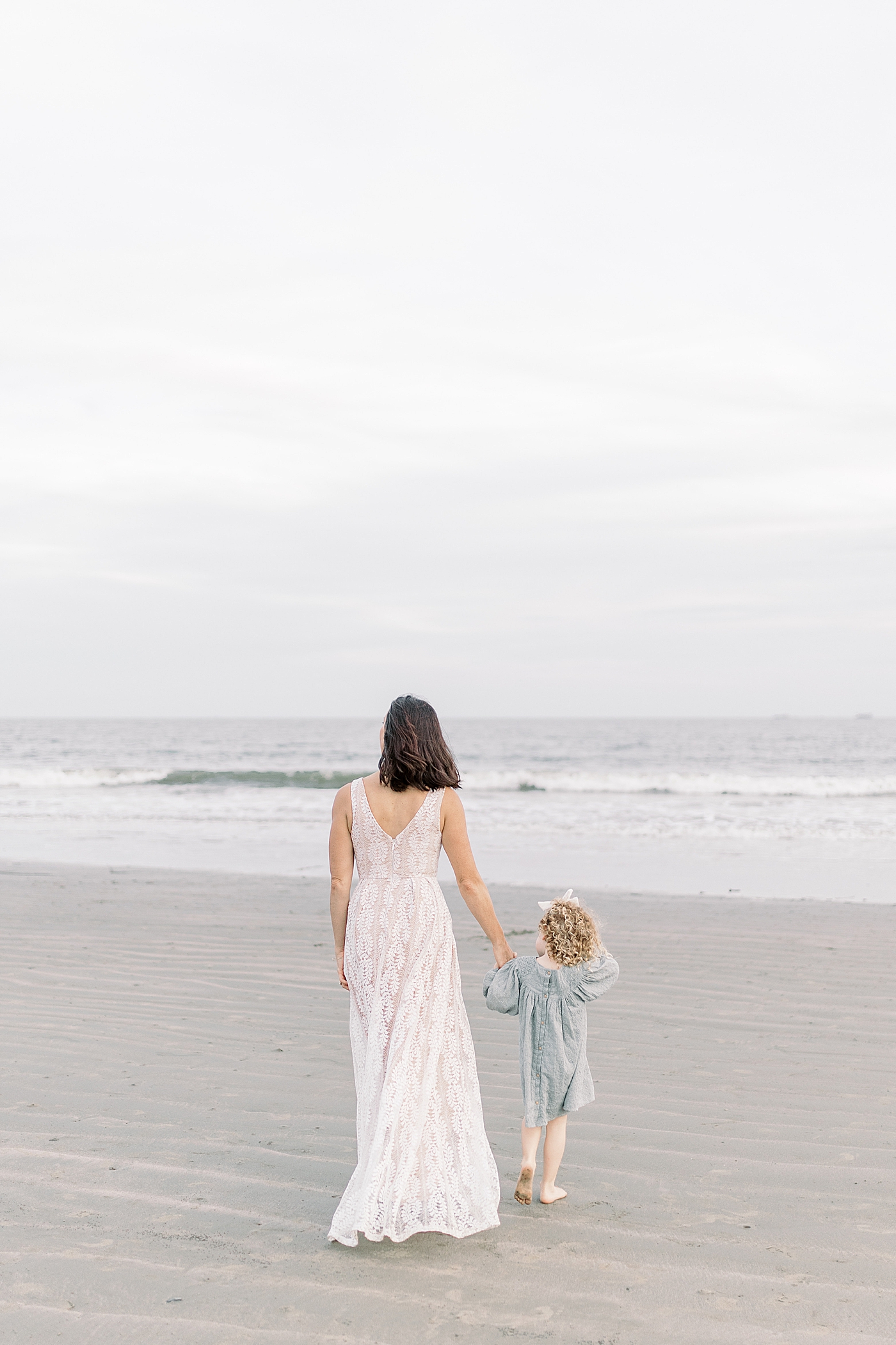 Mom holding her little girl's hand as they walk toward the beach | Photo by Caitlyn Motycka Photography
