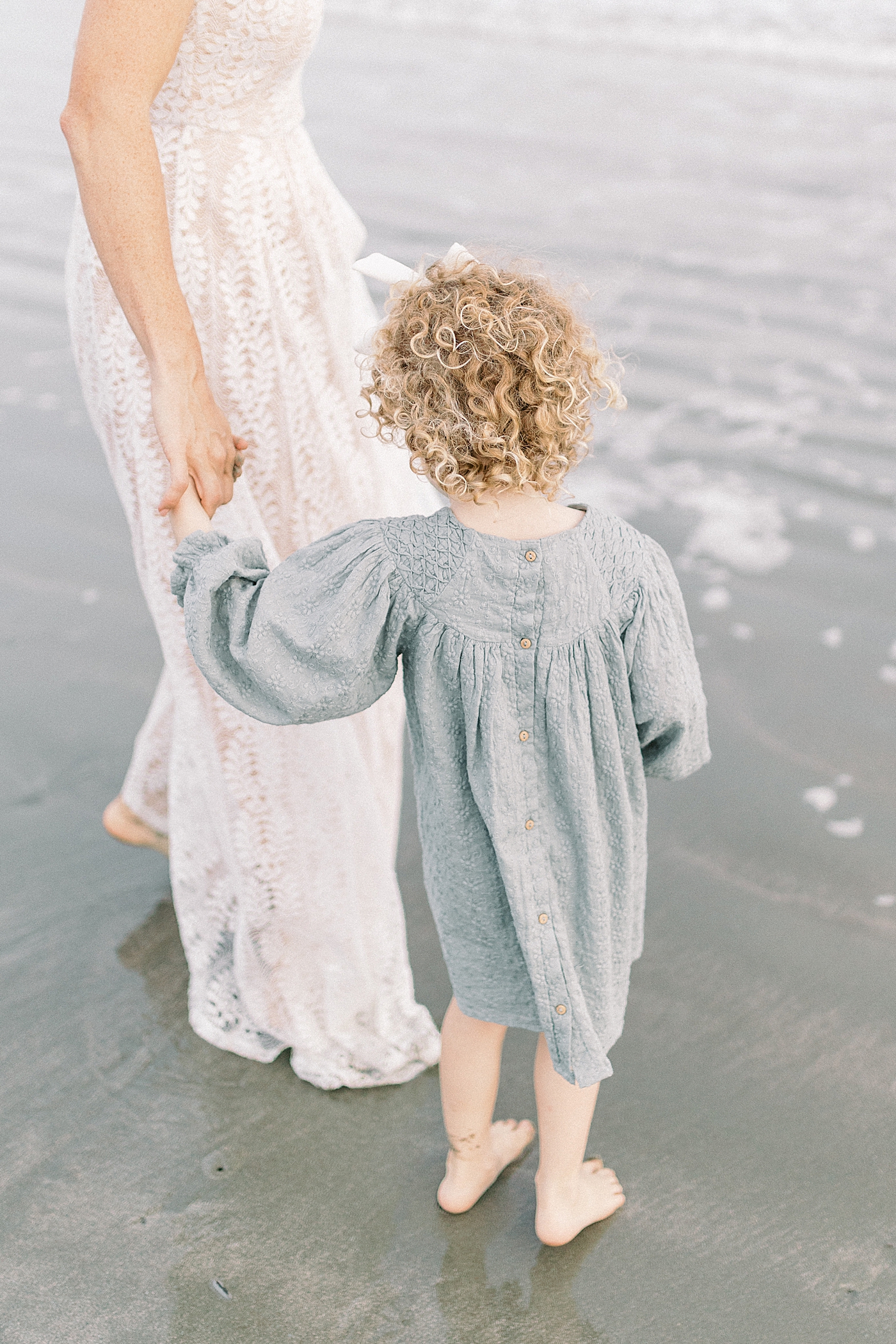 Mom and daughter walking near the water during fall family session at beach | Photo by Caitlyn Motycka Photography