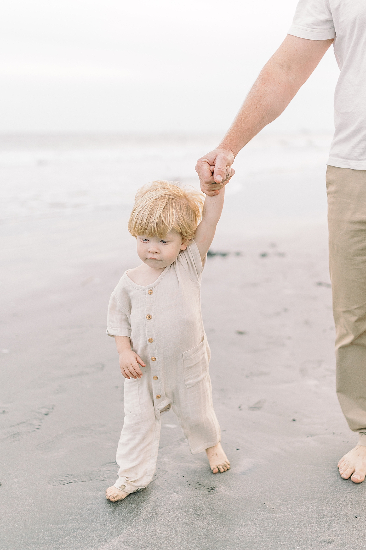 Dad holding baby boys hand during fall family session at beach | Photo by Caitlyn Motycka Photography