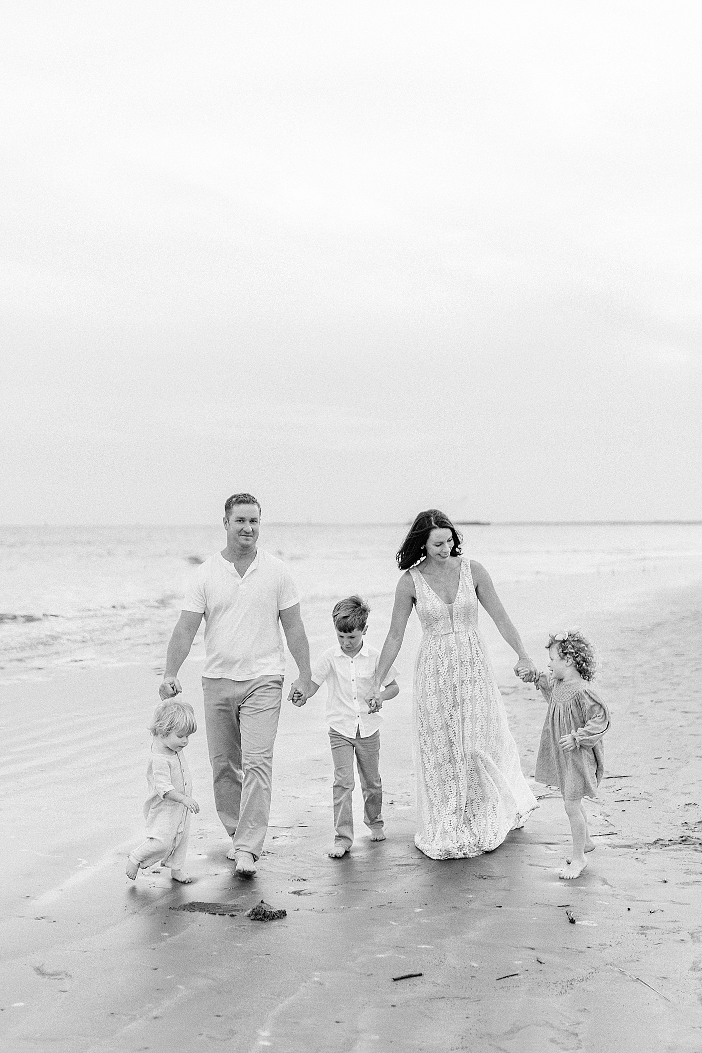 Black and white photo of family walking hand in hand on the beach | Photo by Caitlyn Motycka Photography