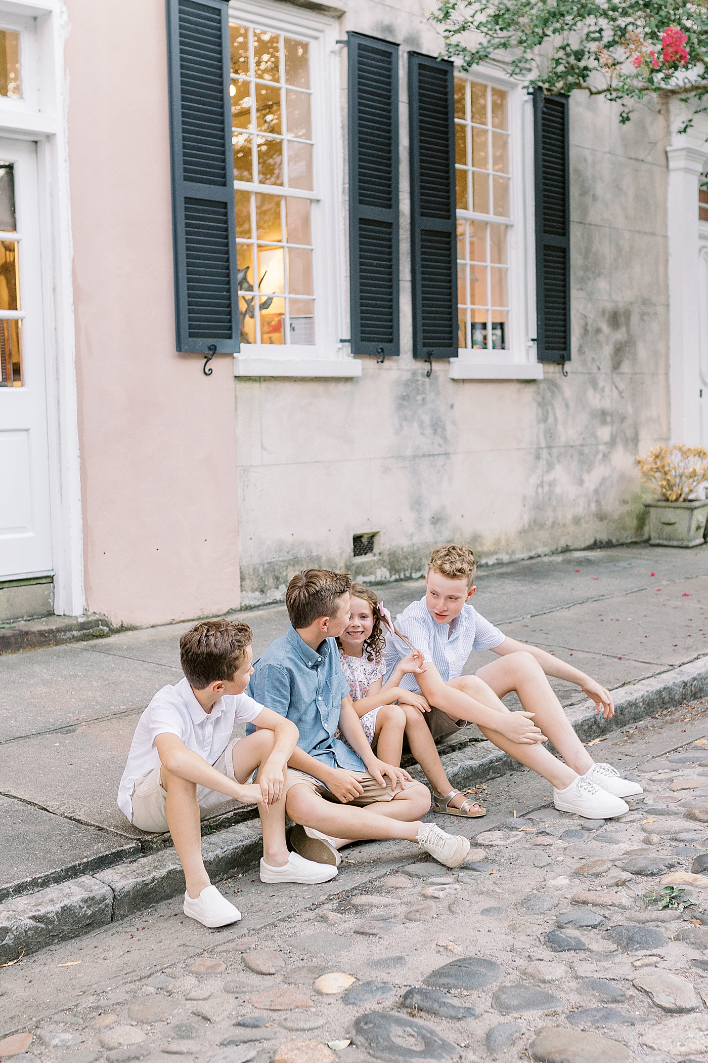 Siblings laughing together sitting near the sidewalk | Photo by Caitlyn Motycka Photography