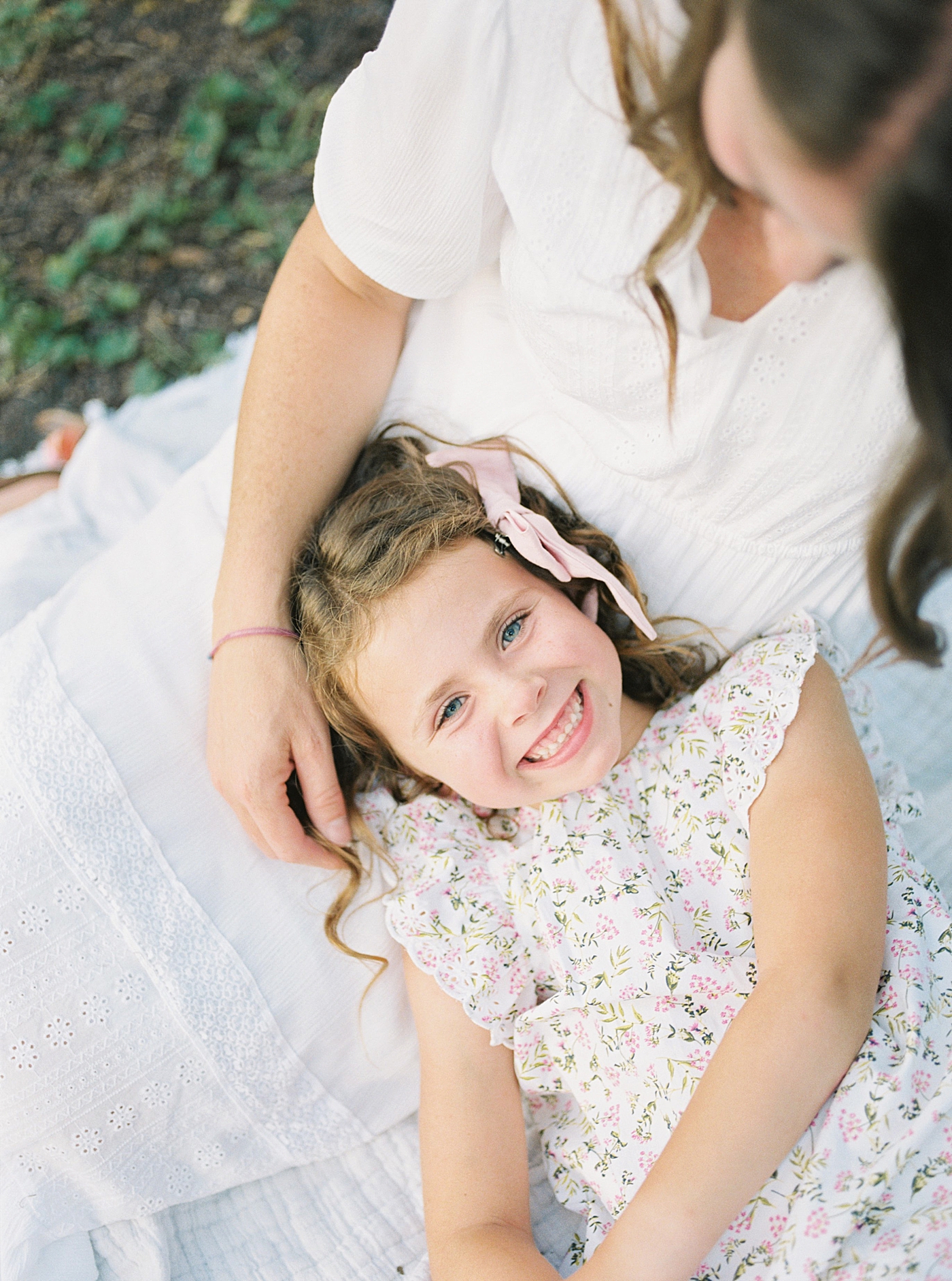 Little girl smiling at the camera laying in mom's lap | Photo by Caitlyn Motycka Photography