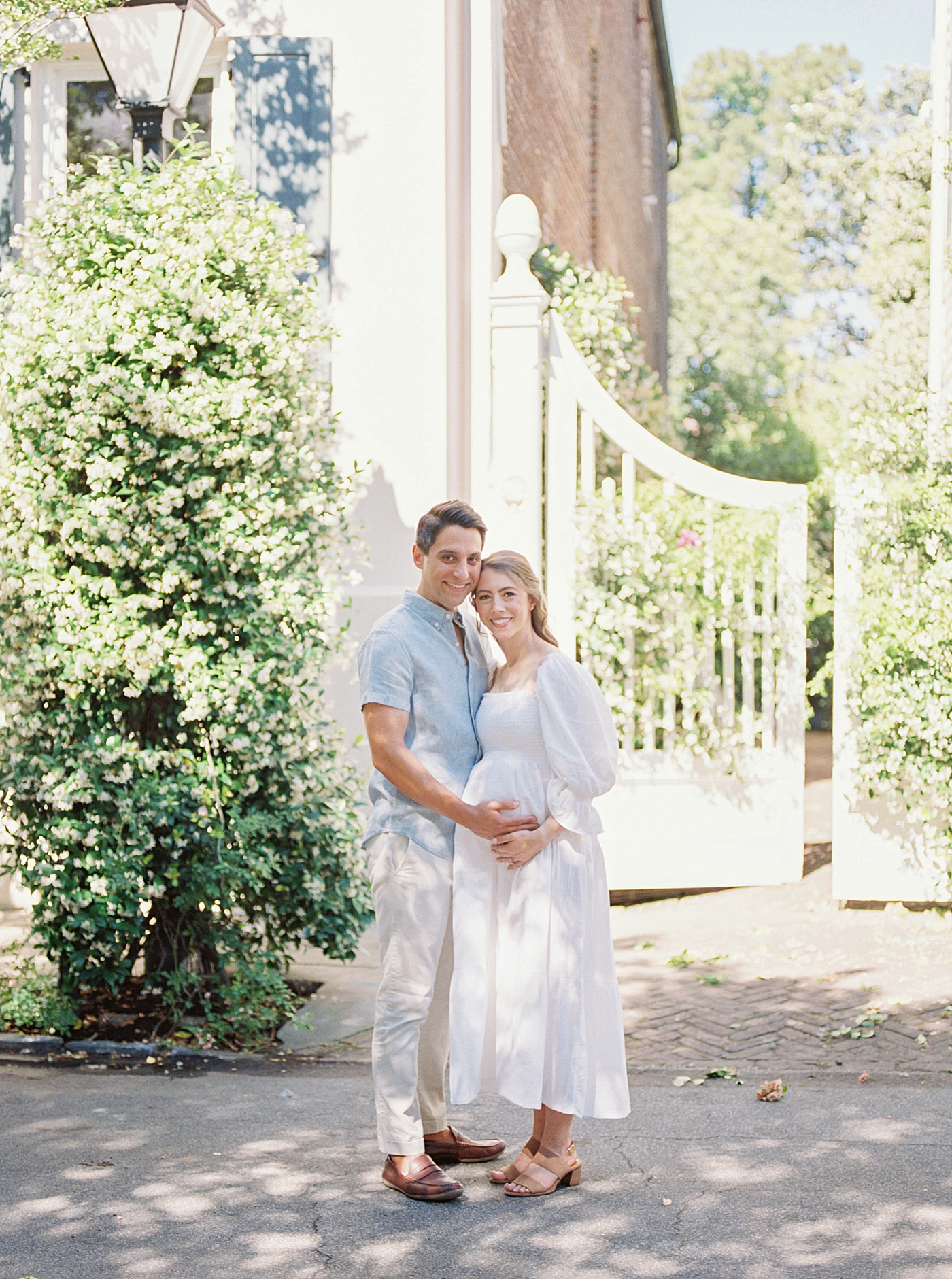 Mother and father to be standing in front of a gate covered in jasmine | Photo by Charleston Film Photographer Caitlyn Motycka