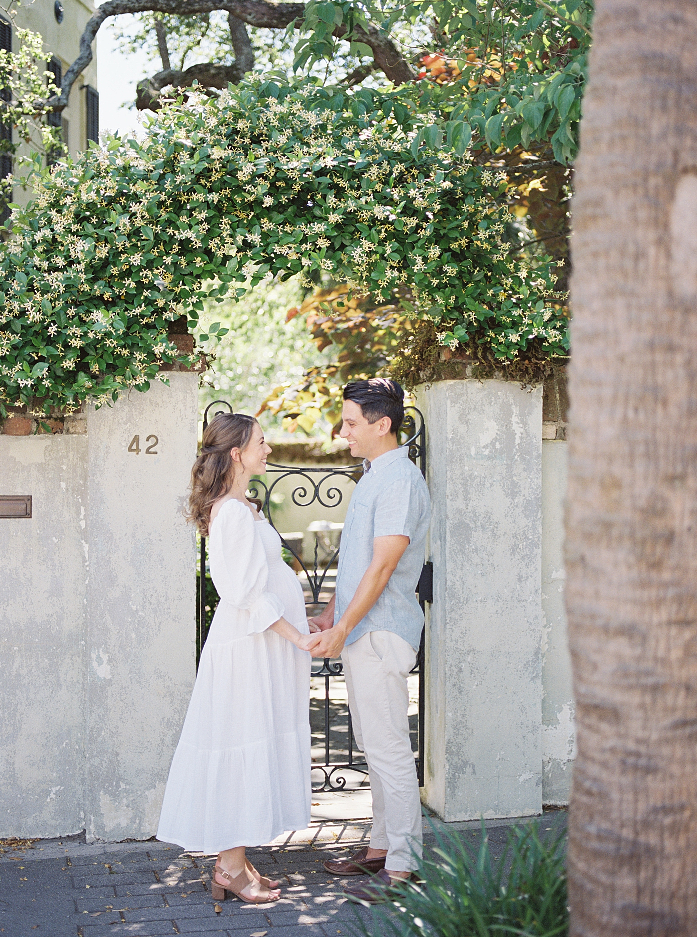 Mom and dad to be holding hands in front of an iron gate | Photo by Charleston Film Photographer Caitlyn Motycka