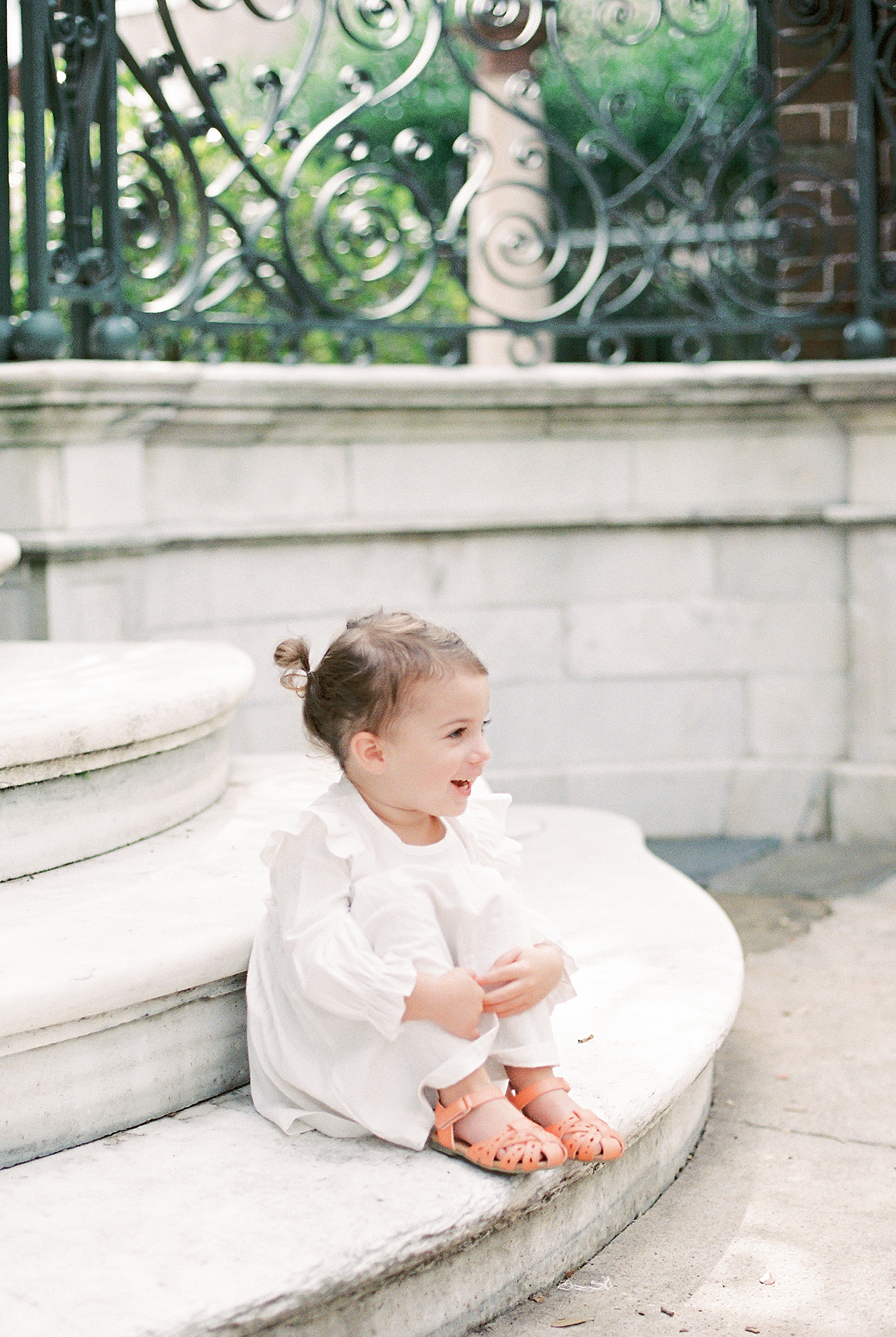 Toddler girl in a white dress sitting on a stoop | Photo by Caitlyn Motycka Photography