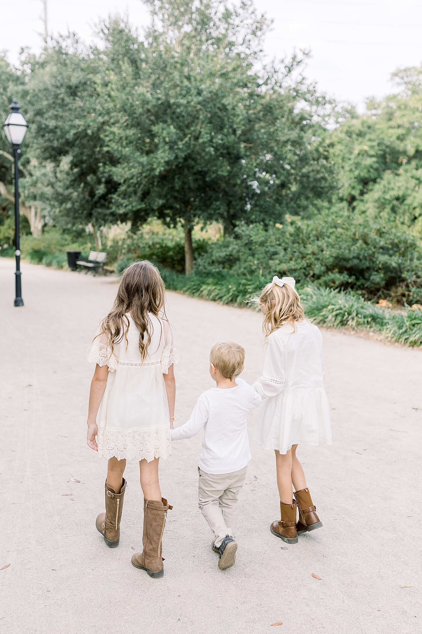 Three siblings holding hands walking through the park during their Fall Family Photos in Charleston | Photo by Caitlyn Motycka Photography