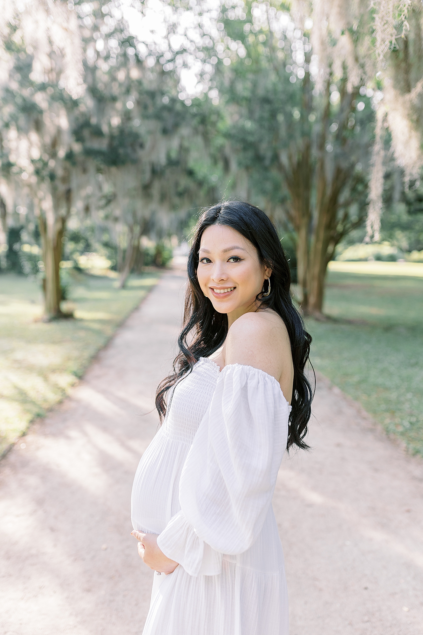 Smiling mother to be in a white dress during her maternity photos in Charleston | Photo by Caitlyn Motycka Photography