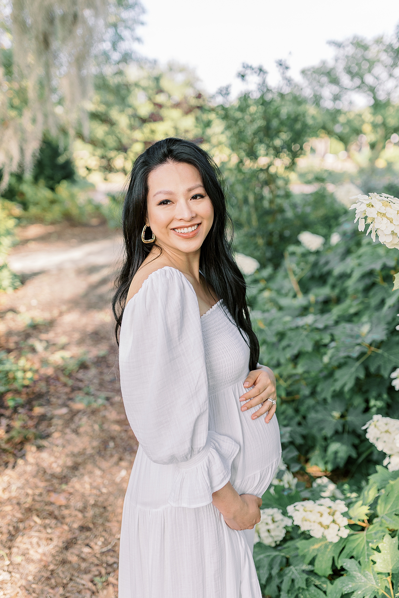 Mother to be in a white dress holding her belly | Photo by Caitlyn Motycka Photography
