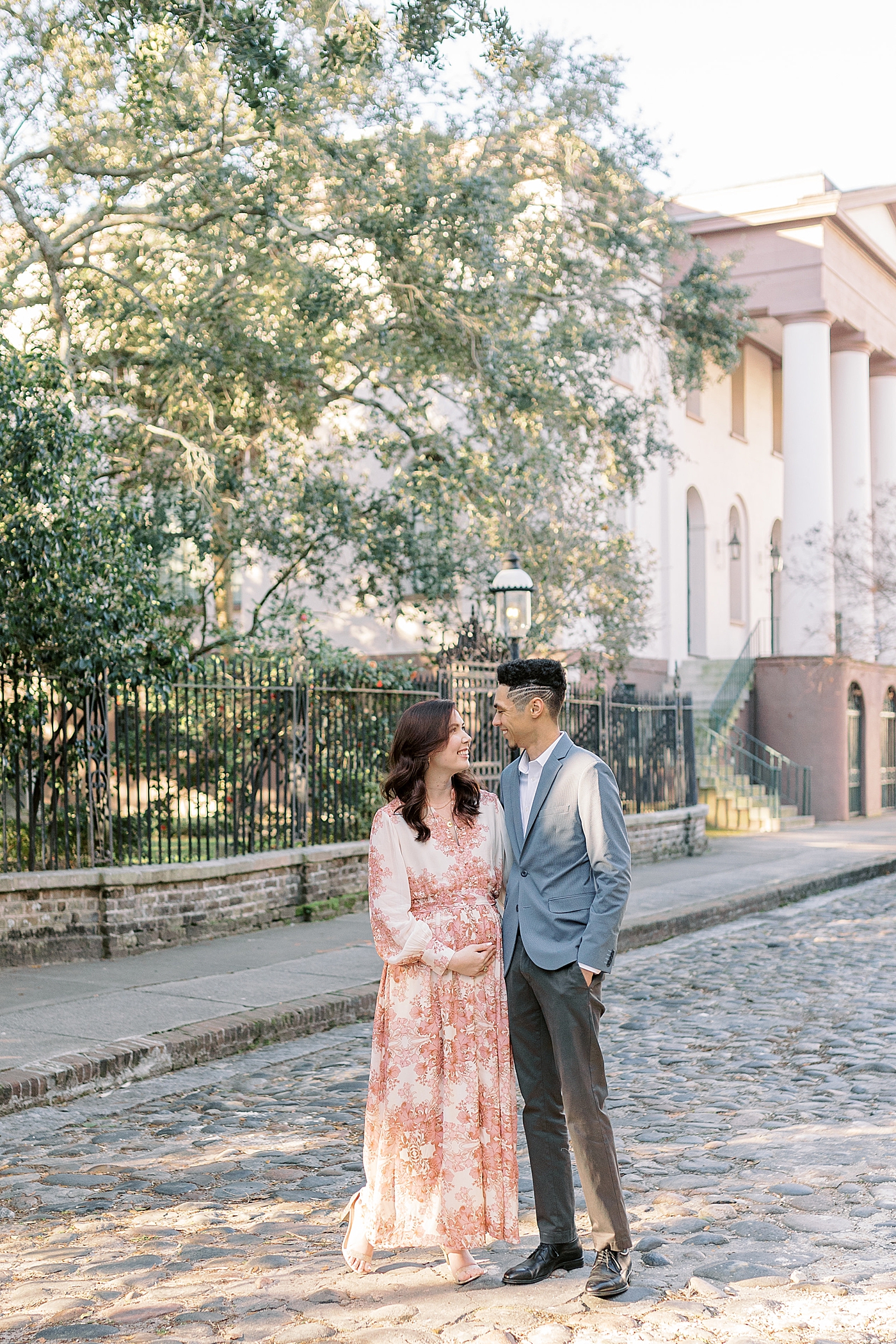 Mom and dad to be on a cobblestone street during their Pregnancy Announcement in Downtown Charleston | Photo by Caitlyn Motycka Photography