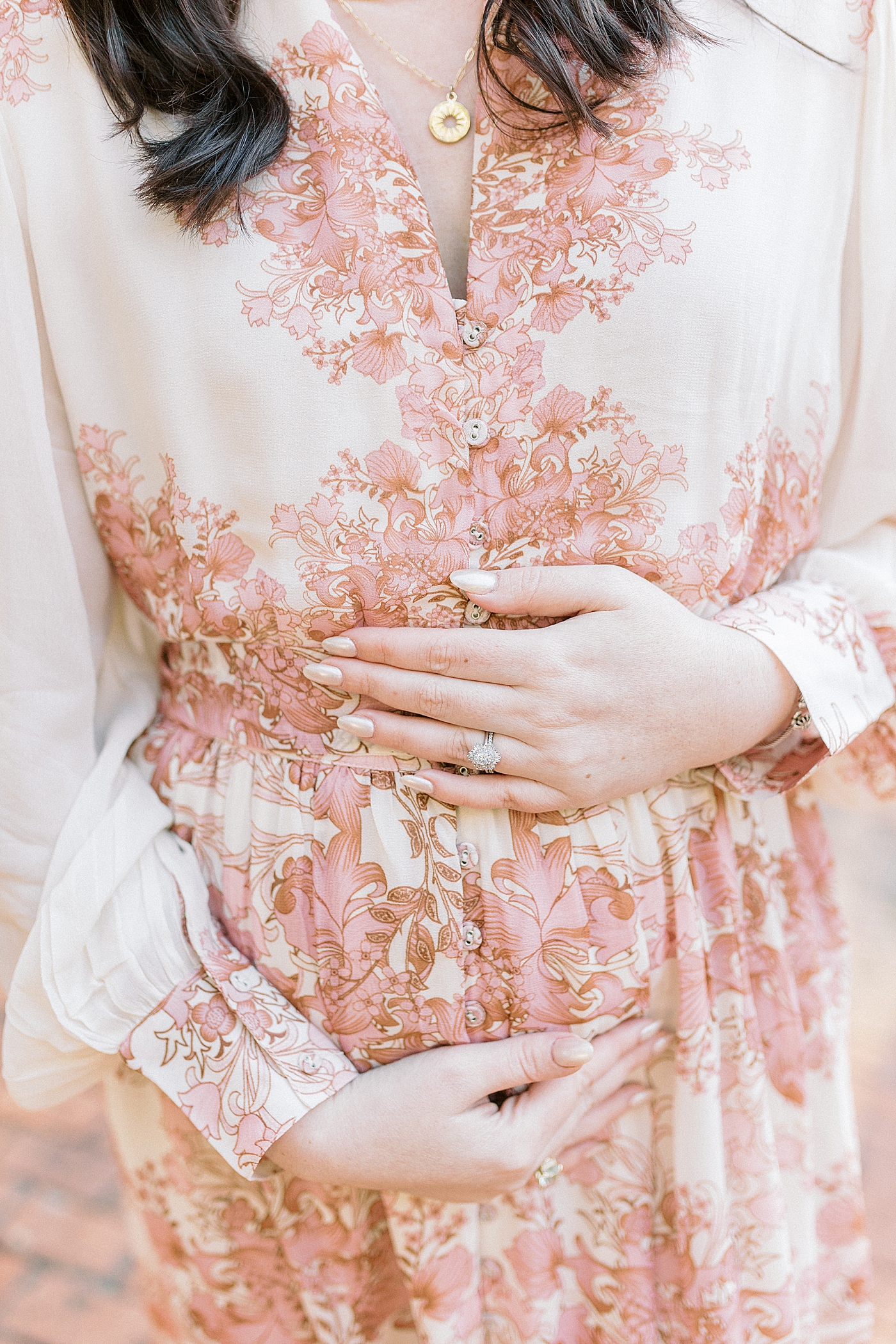 Mother to be in pink floral dress cradling her belly | Photo by Caitlyn Motycka Photography
