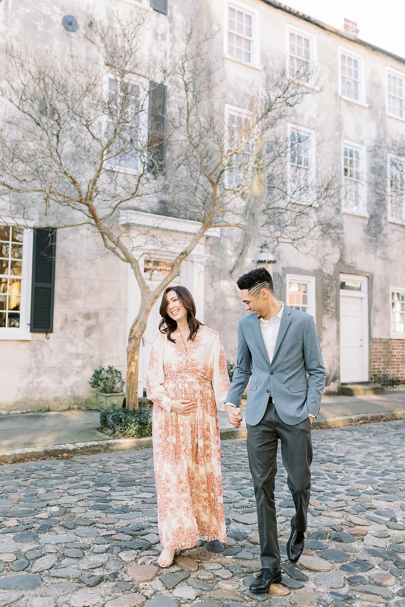 Couple smiling holding hands walking down a cobblestone street in Charleston, SC | Photo by Caitlyn Motycka Photography