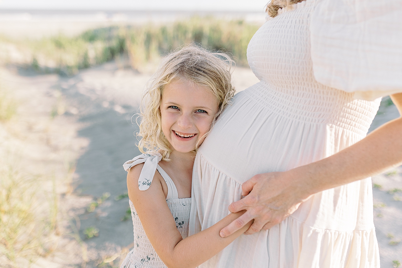 Little girl snuggling her mom's belly during Maternity Session at Folly Beach | Image by Caitlyn Motycka