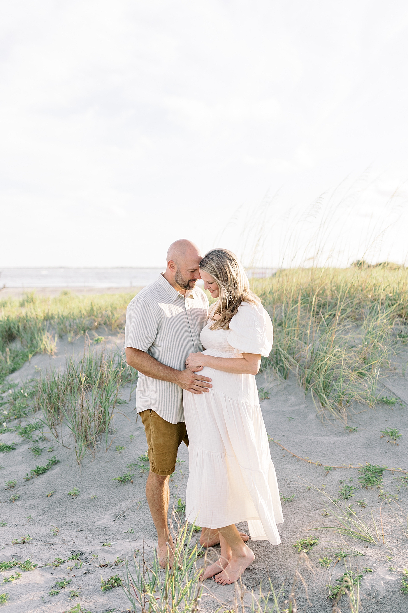 Mom and dad to be snuggling during their Maternity Session at Folly Beach | Image by Caitlyn Motycka