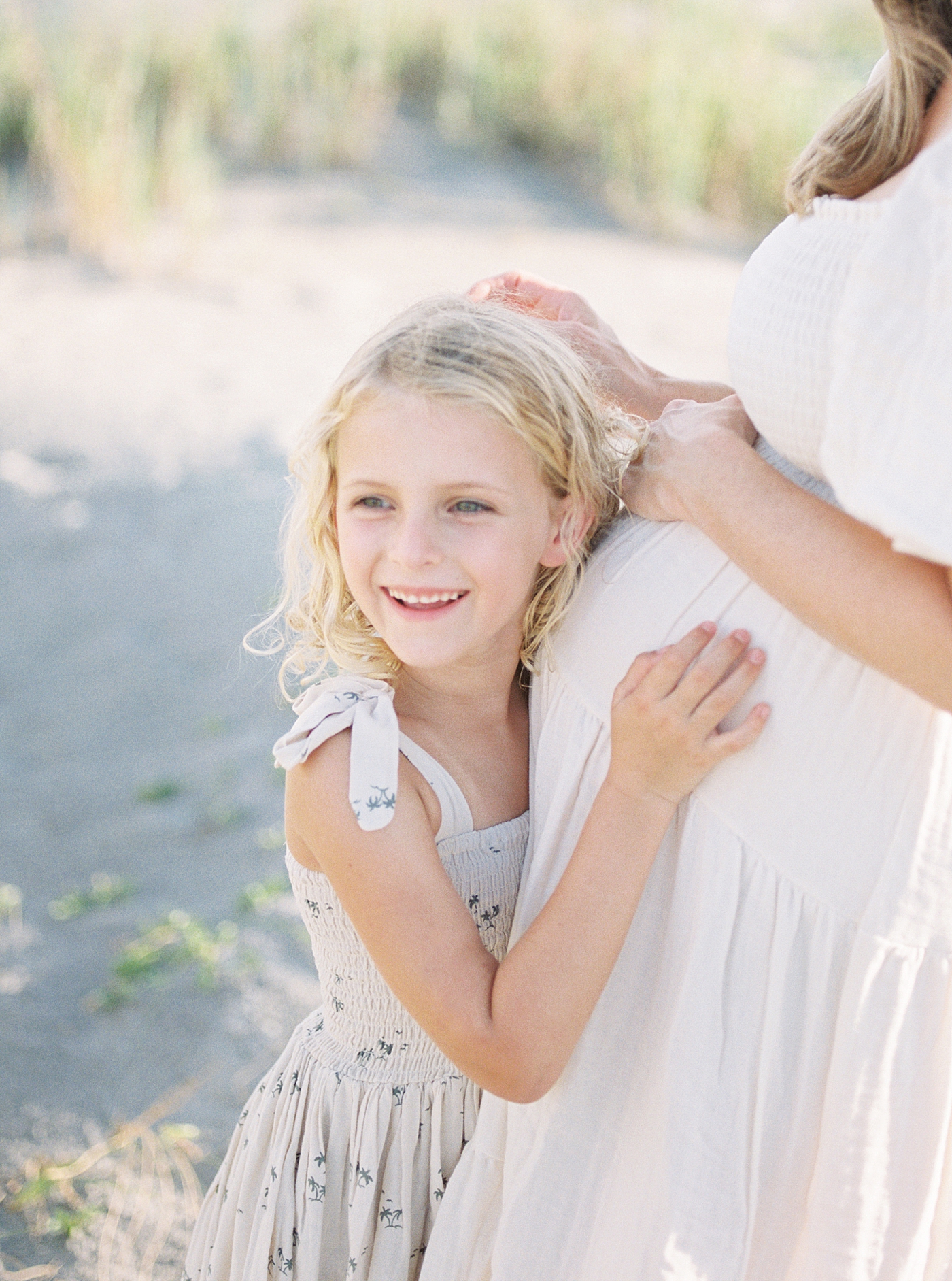 Mom brushing back little girl's blonde hair during their Maternity Session at Folly Beach | Image by Caitlyn Motycka