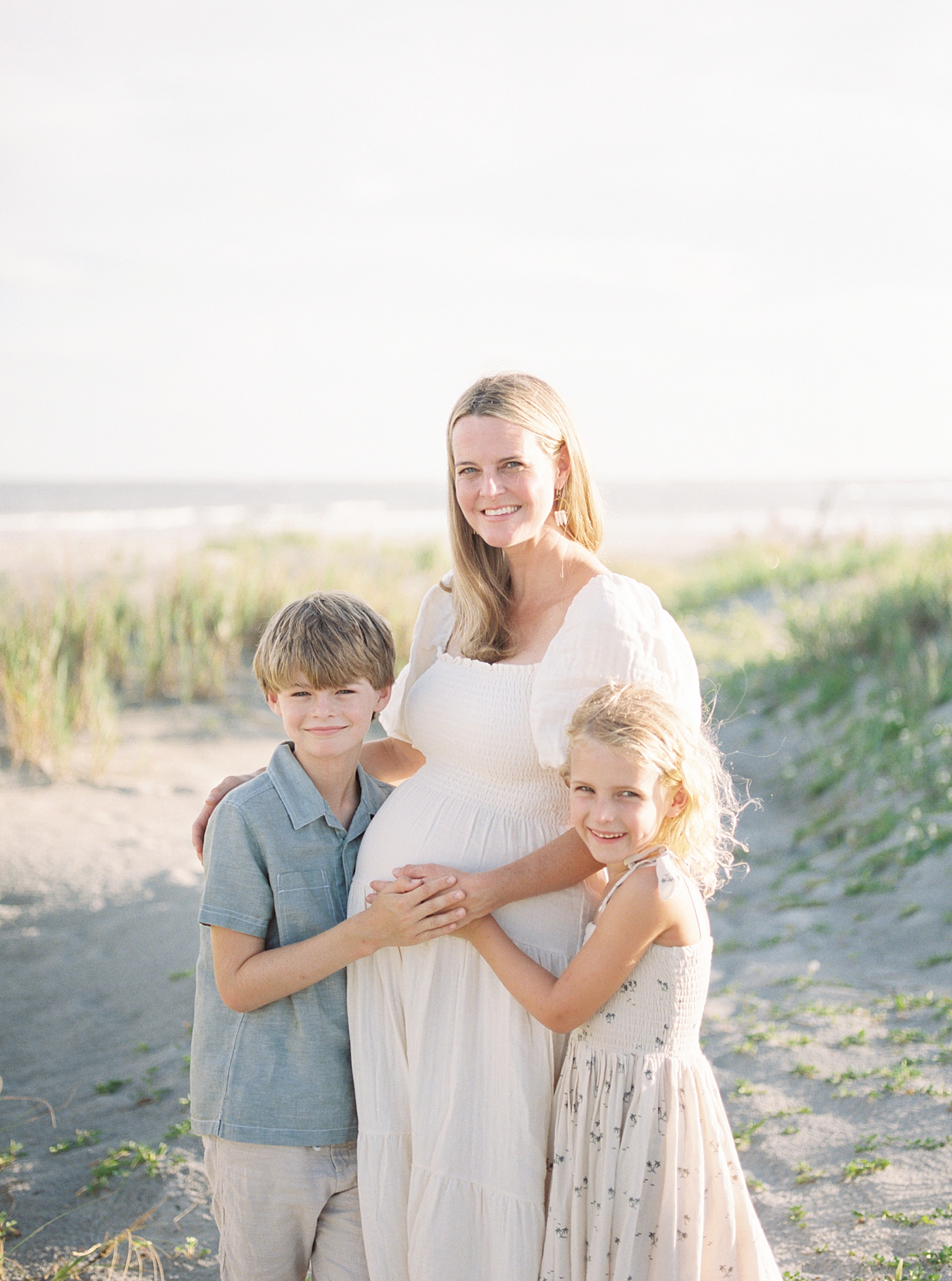 Mom to be with her two kids smiling during their Maternity Session at Folly Beach | Image by Caitlyn Motycka