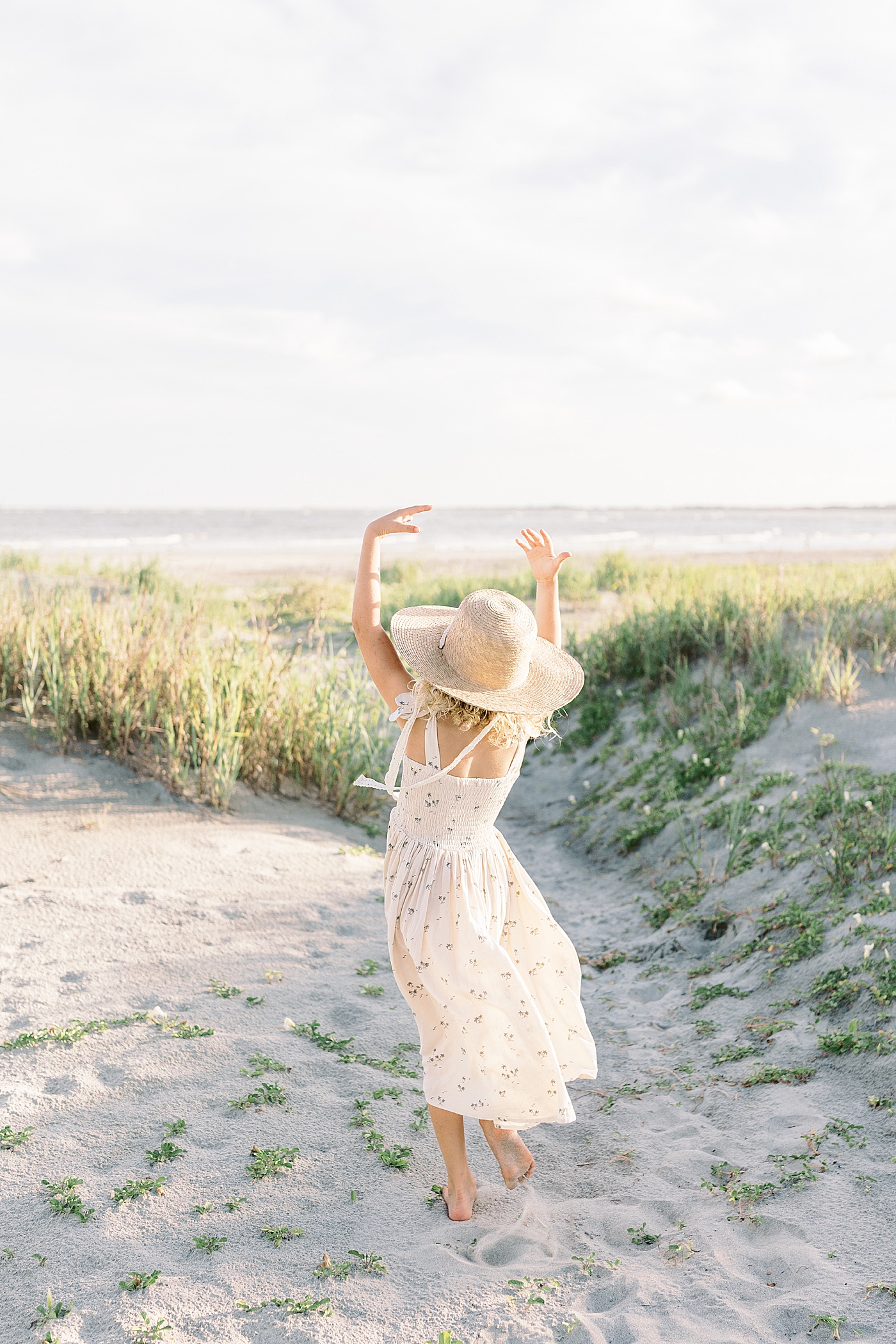 Little girl in a floral dress and hat twirling on the beach | Image by Caitlyn Motycka