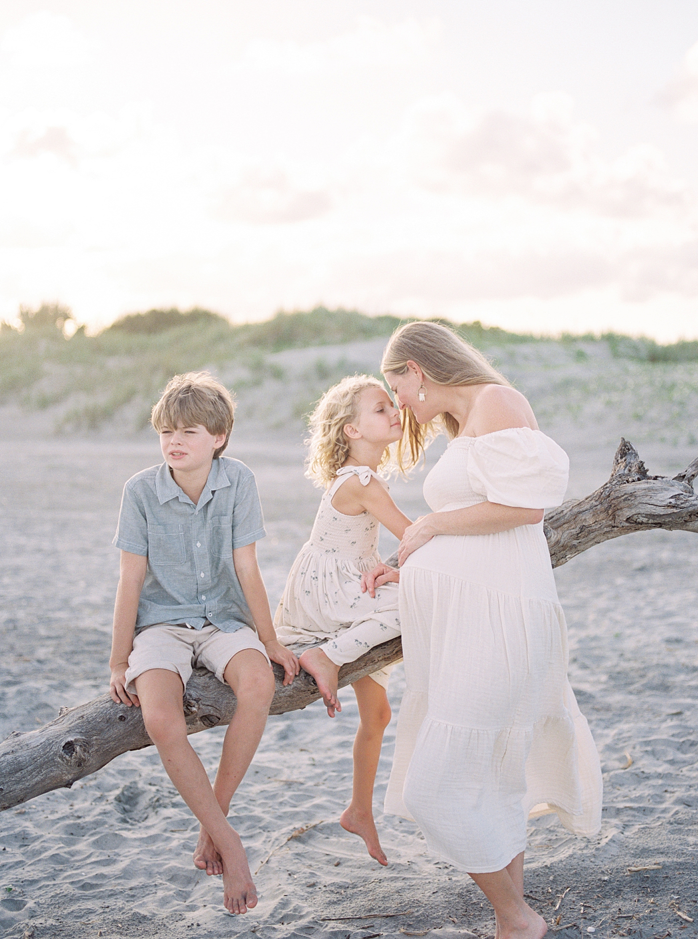 Mom and little kids interacting sitting on a fallen tree at the beach | Image by Caitlyn Motycka