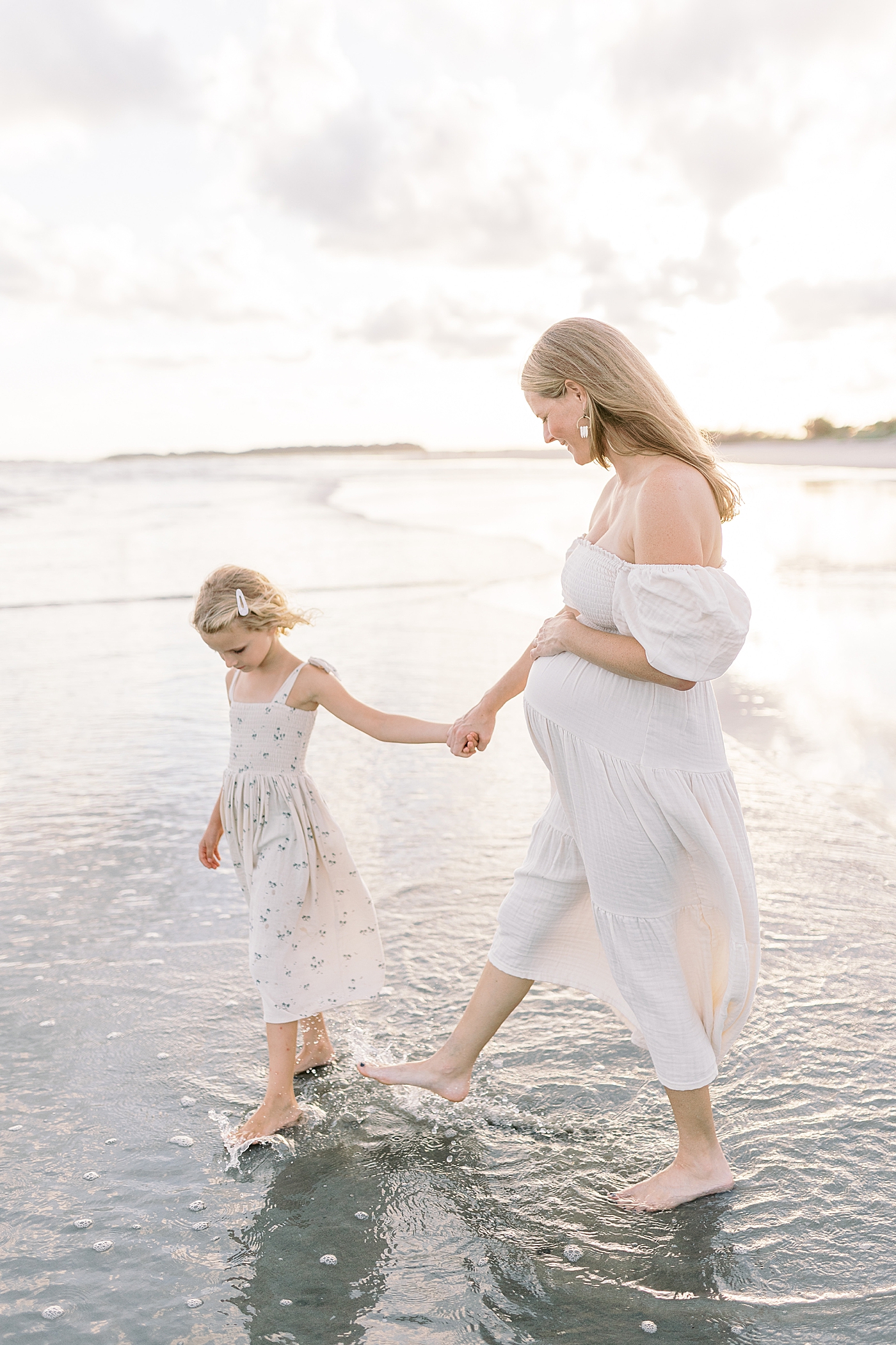 Mom and little girl holding hands walking along the water during their Maternity Session at Folly Beach | Image by Caitlyn Motycka