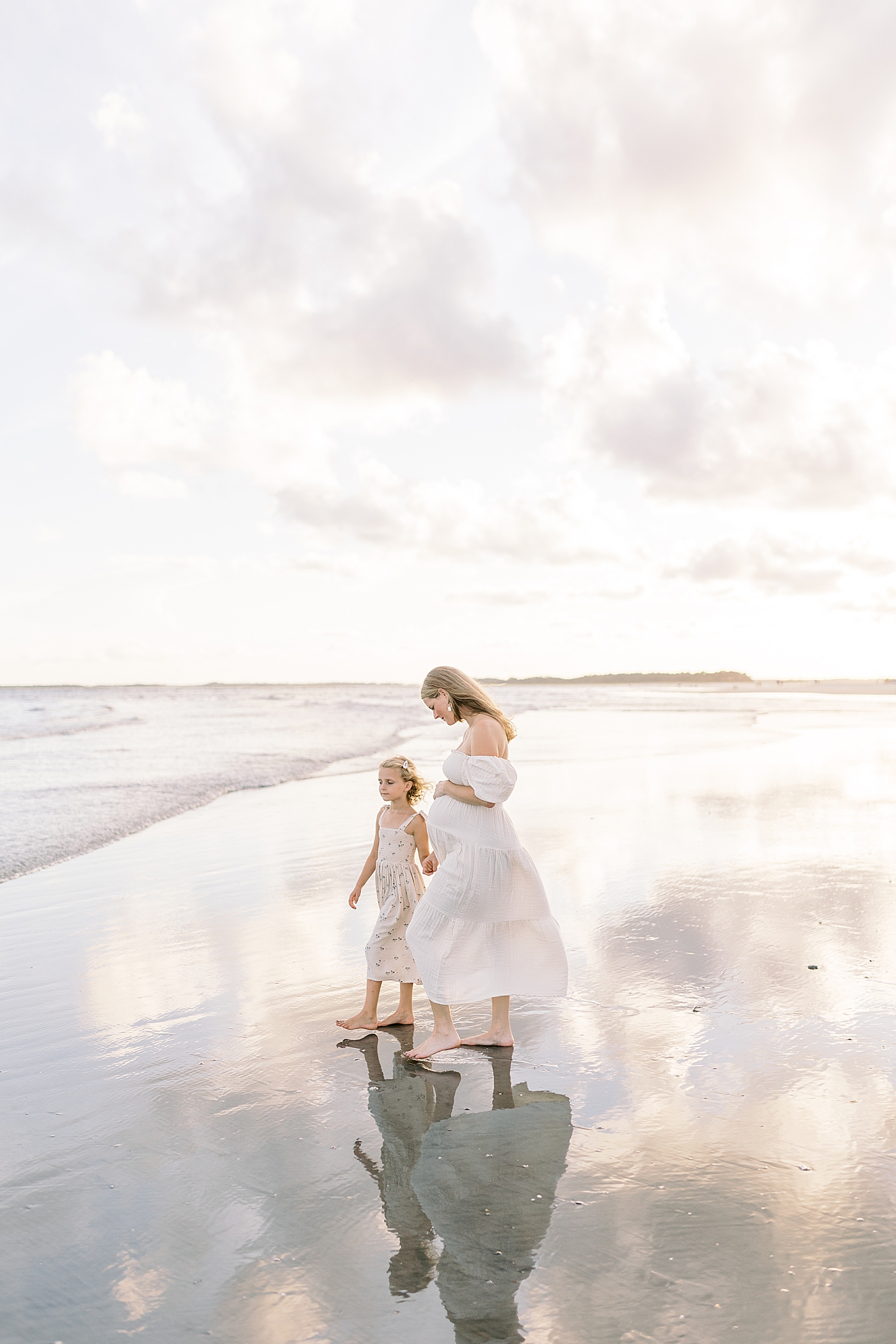 Mom to be and little girl walking on the beach | Image by Caitlyn Motycka