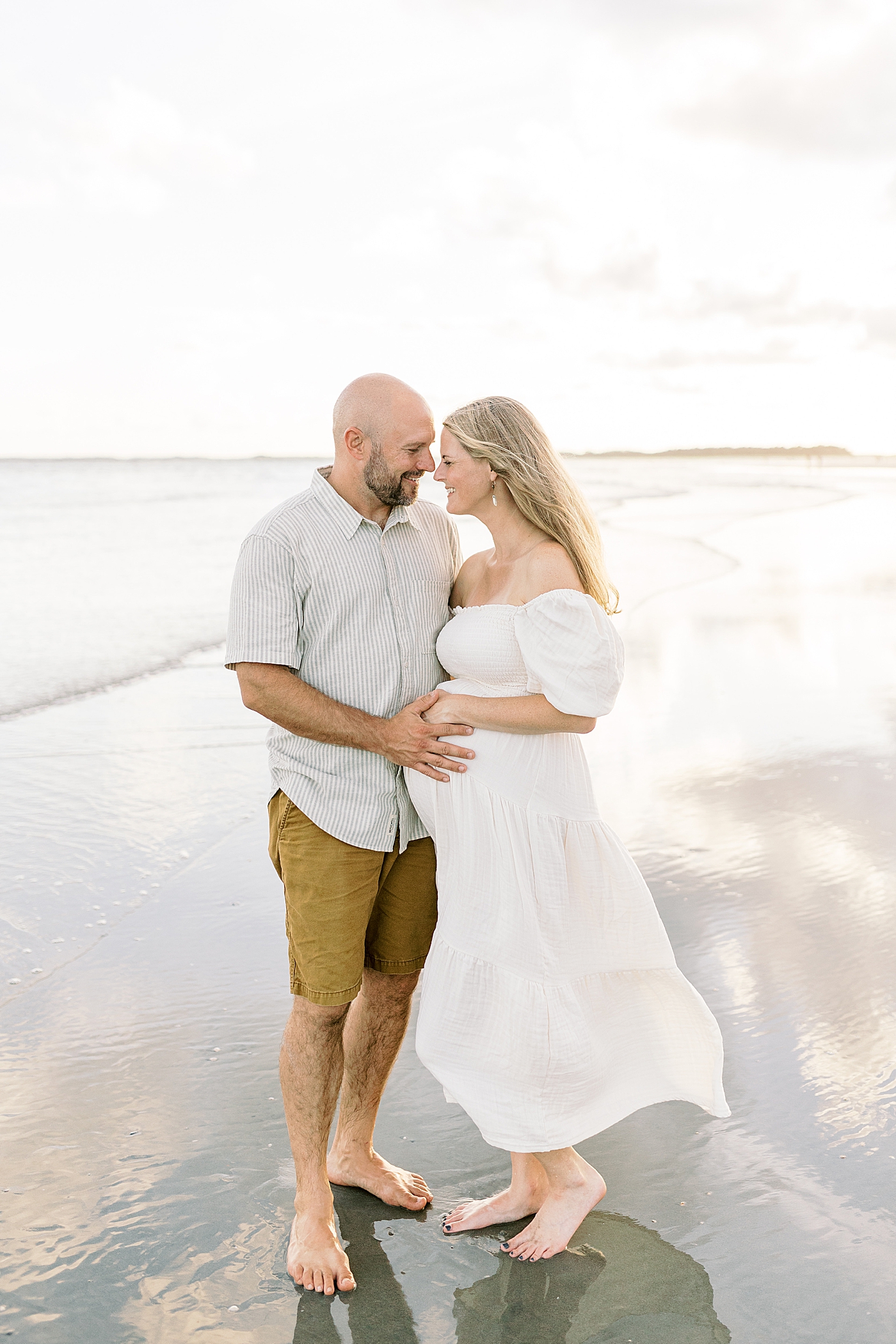 Mom and dad to be standing on the beach during their Maternity Session at Folly Beach | Image by Caitlyn Motycka