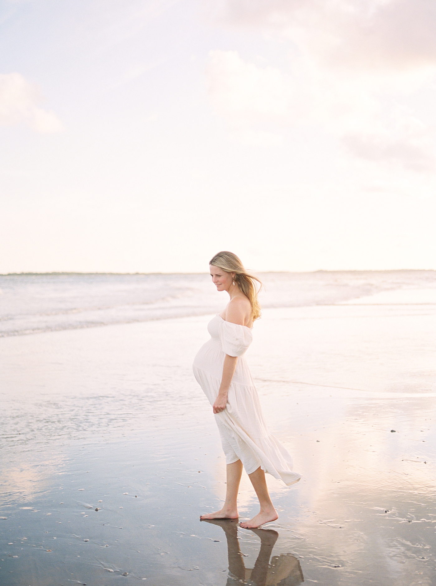 Mom to be in long white dress walking to the ocean | Image by Caitlyn Motycka