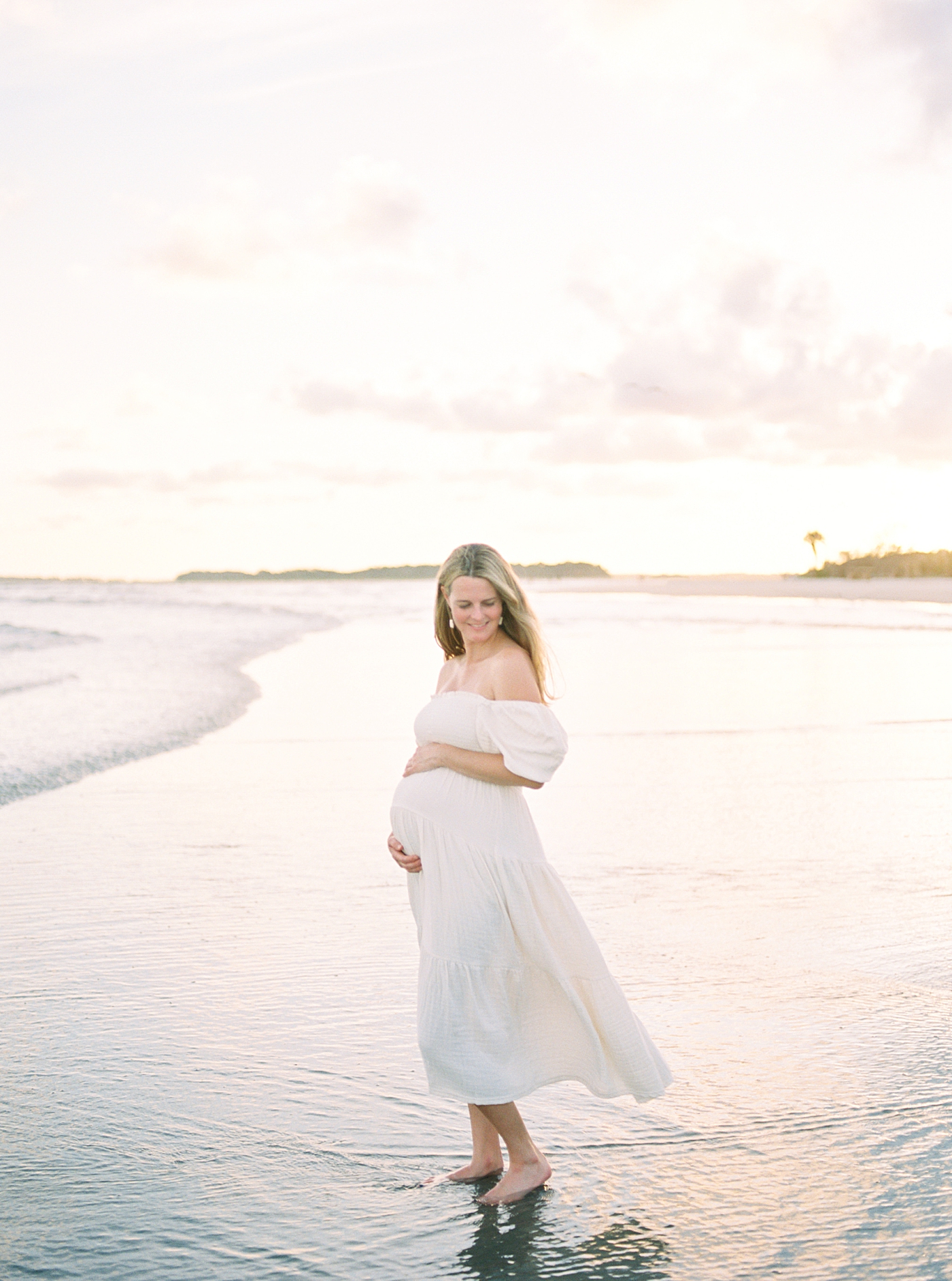 Mom to be in a white dress standing in the ocean at sunset | Image by Caitlyn Motycka