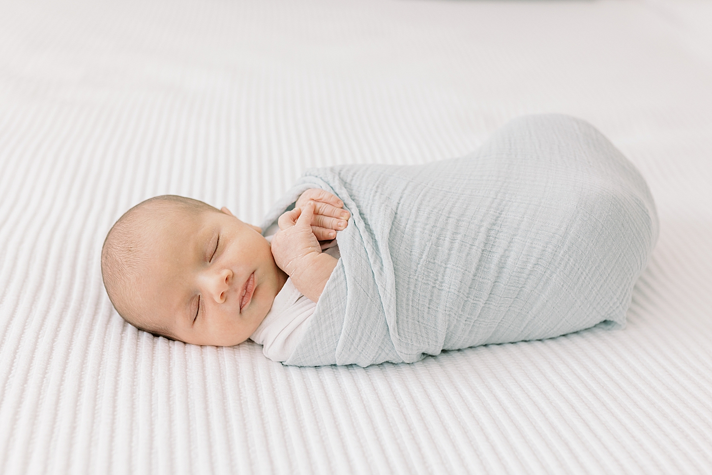 Sleeping baby wrapped in a swaddle during lifestyle newborn photos | Image by Caitlyn Motycka