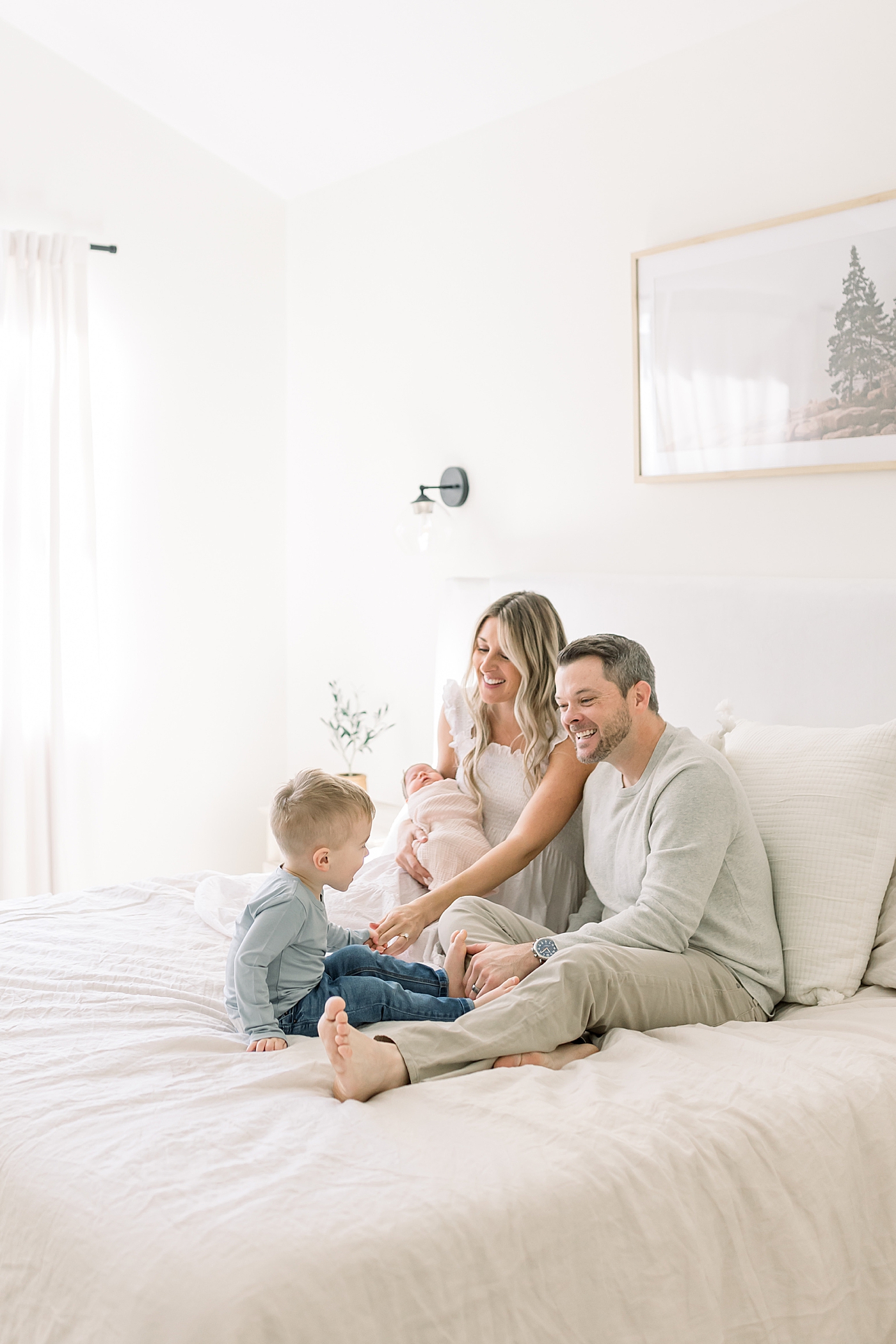 Mom, dad, and toddler sitting on a bed holding their new baby | Newborn Photos with Toddler with Caitlyn Motycka Photography
